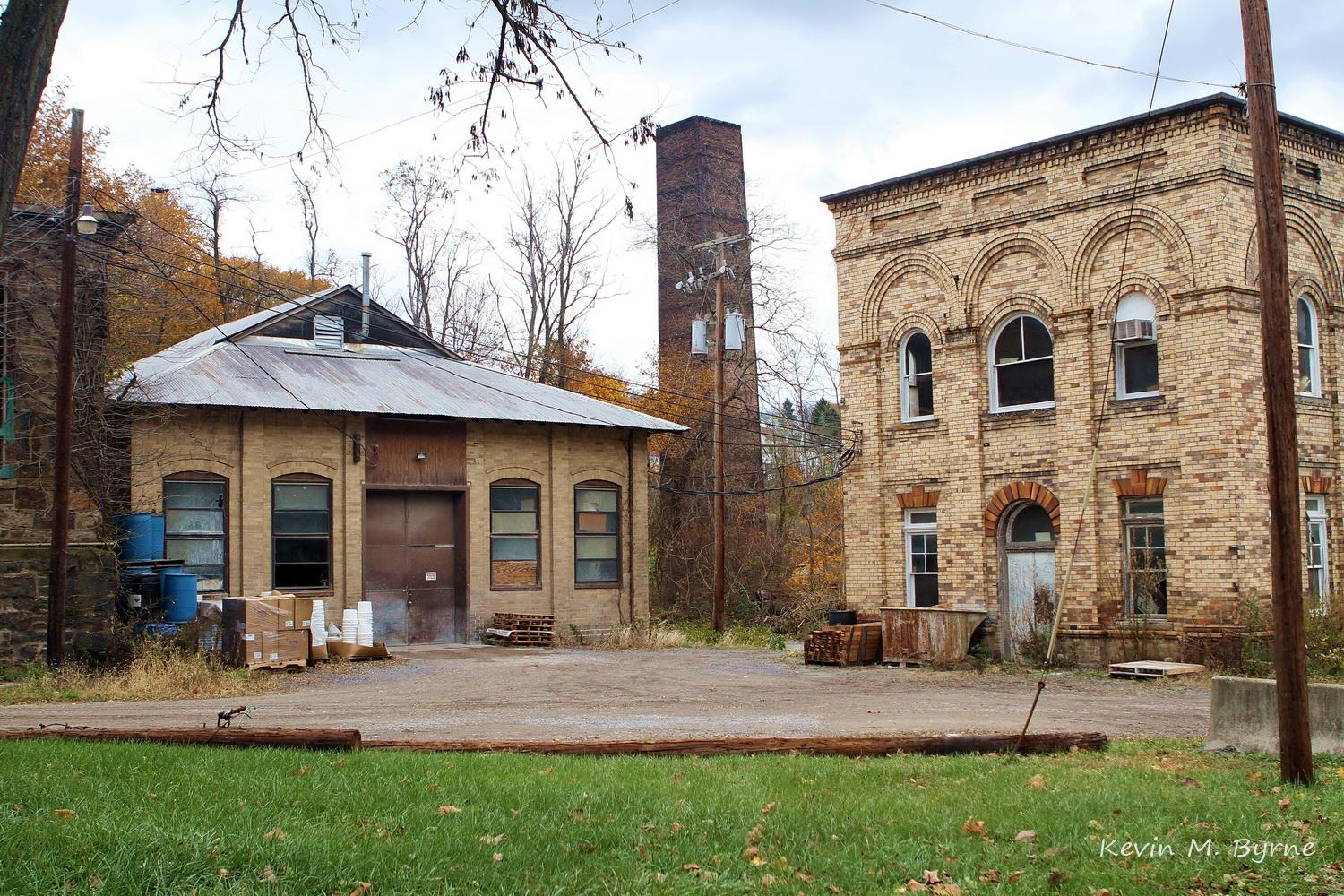 Two old brick industrial buildings and a tall chimney under an overcast sky.