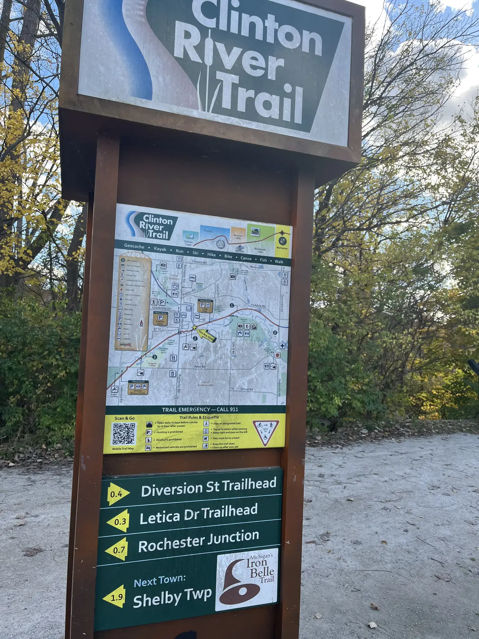 A wooden trail sign with a map stands outdoors among trees.