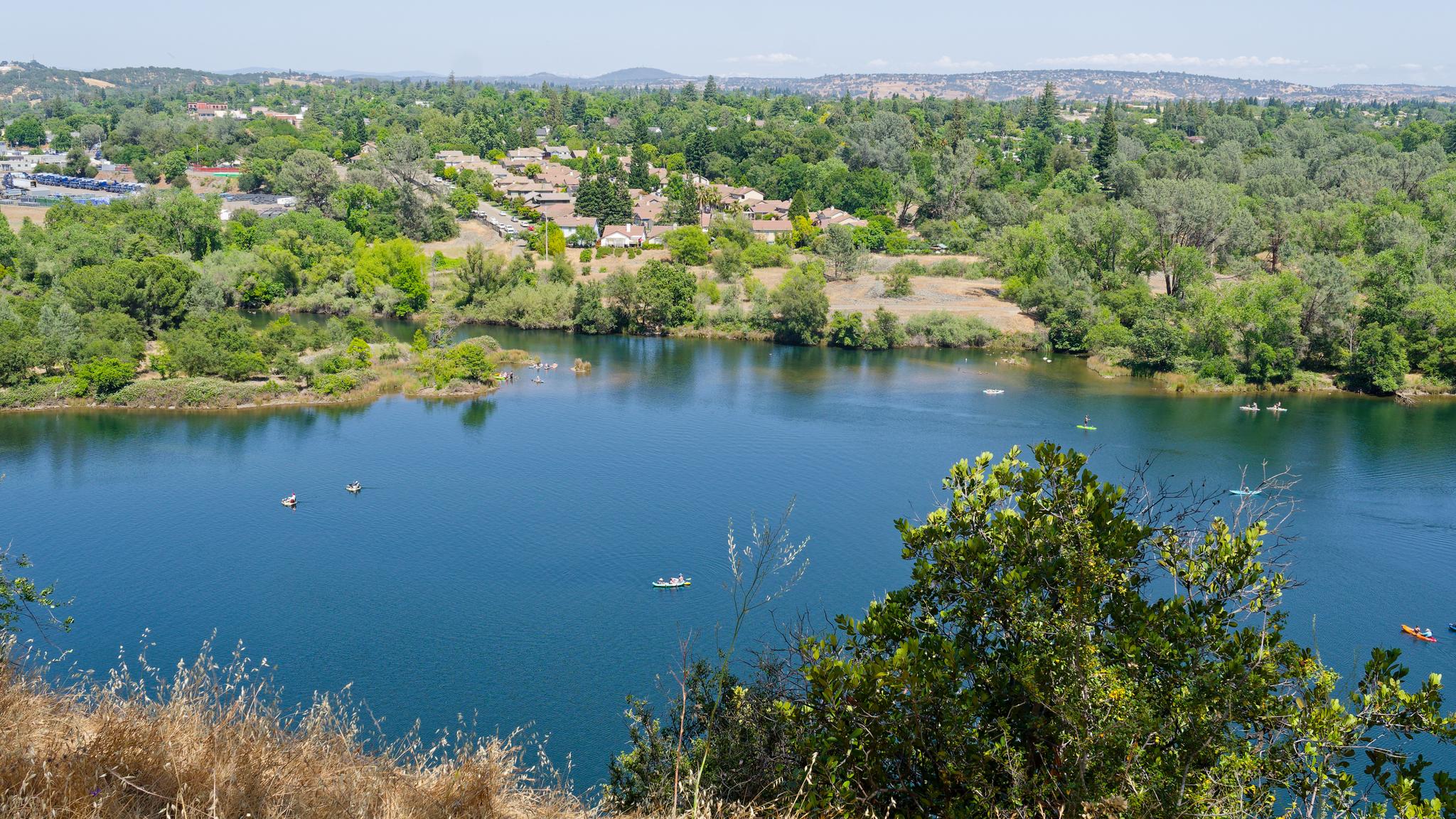 Aerial view of a blue lake with small boats, surrounded by green trees.