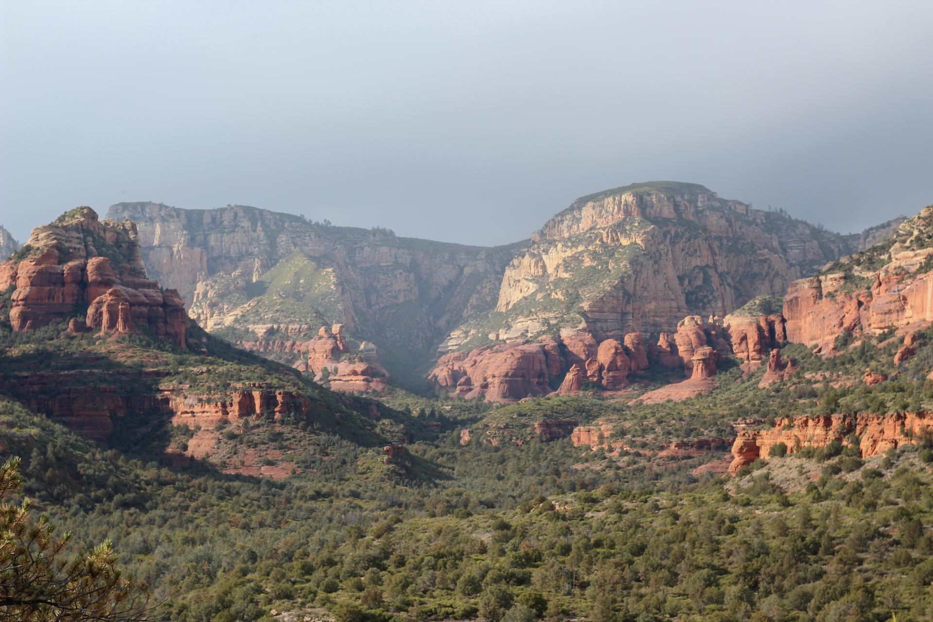 Vast red rock mountains and green valleys under a cloudy sky.