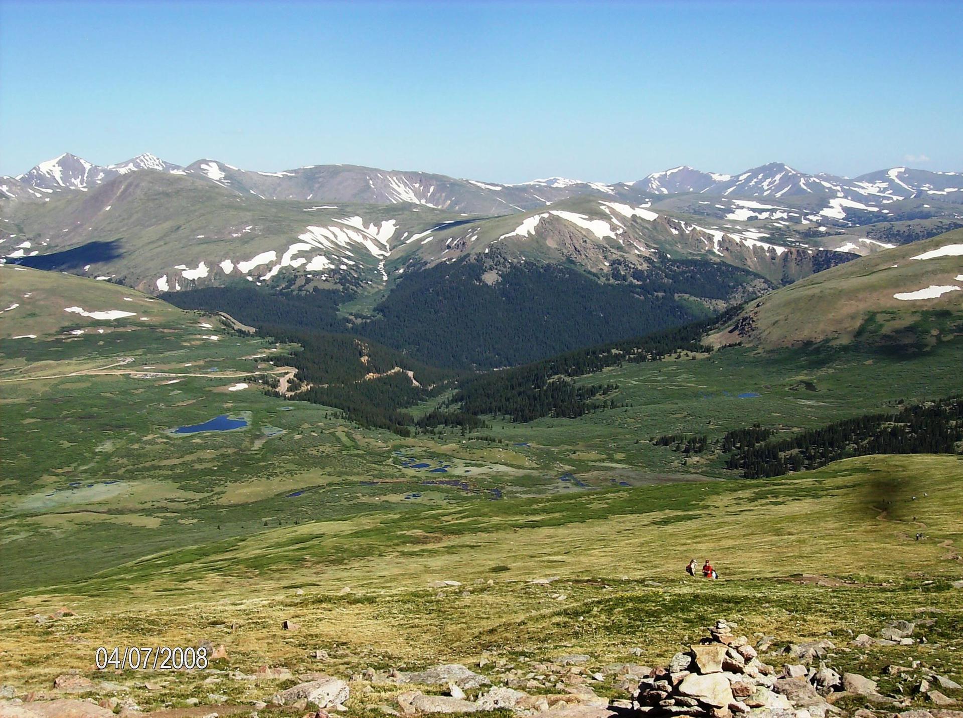 Expansive view of a rugged mountain range with snow patches and green valleys.