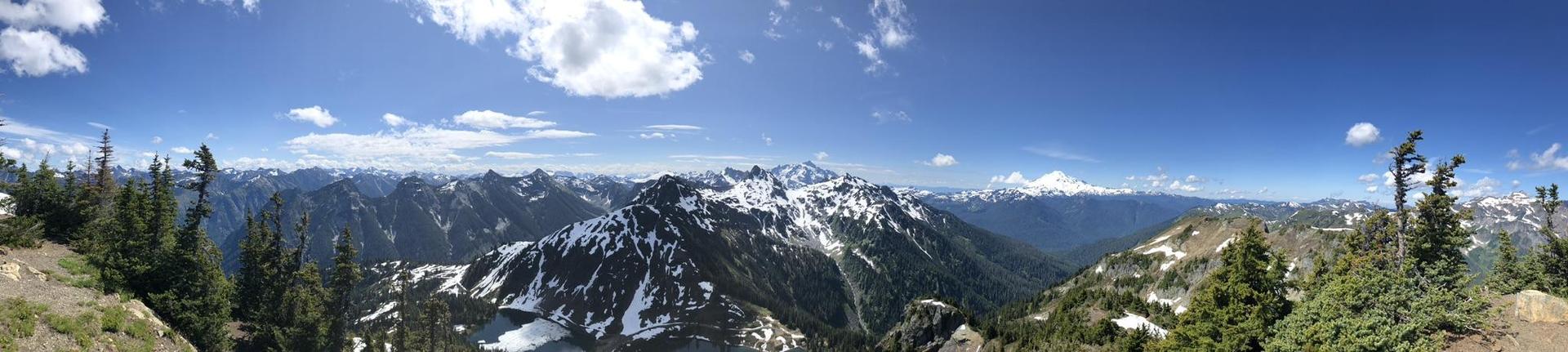 Panoramic view of vast, snow-dusted mountain ranges under a bright blue sky.
