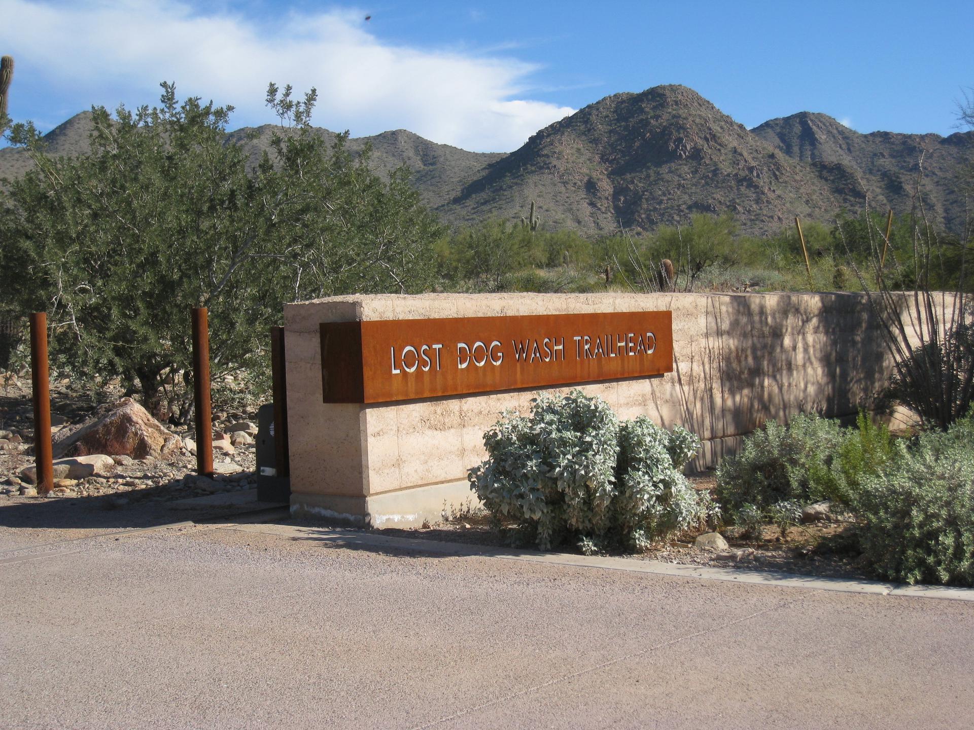 A stone and metal sign at a desert trailhead entrance.