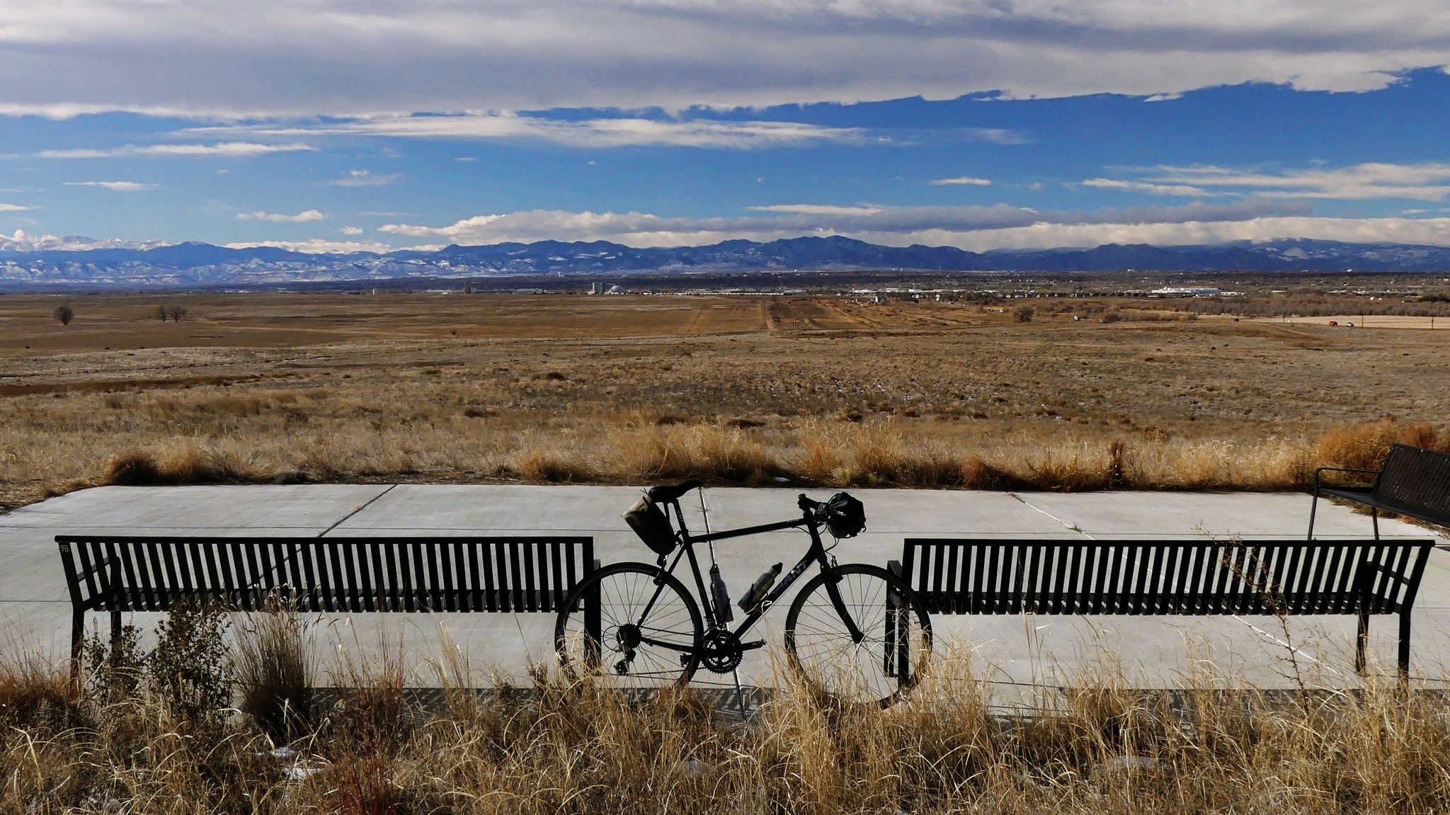 A bicycle rests between two benches overlooking a vast, dry landscape. - Bike loop from Commerce City