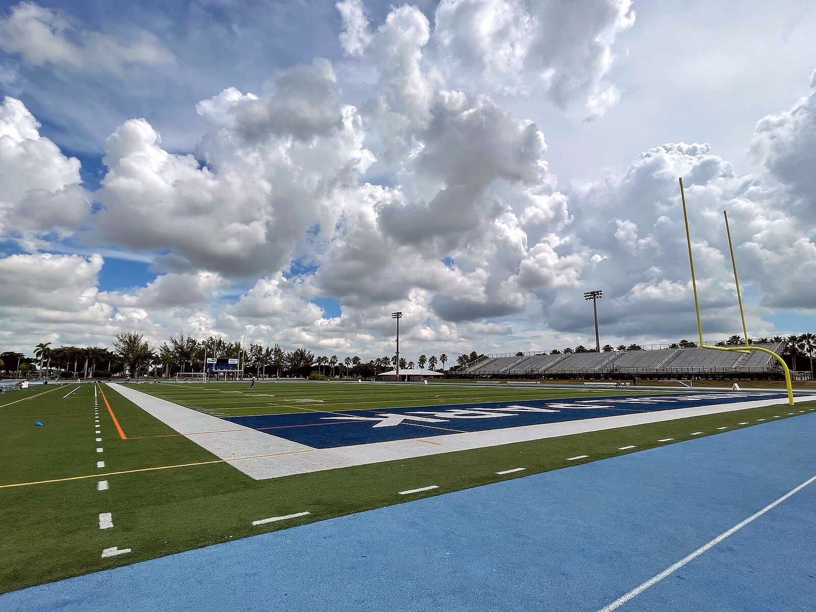 Daytime view of an empty football field and blue track under a cloudy sky. - Tropical Park loop