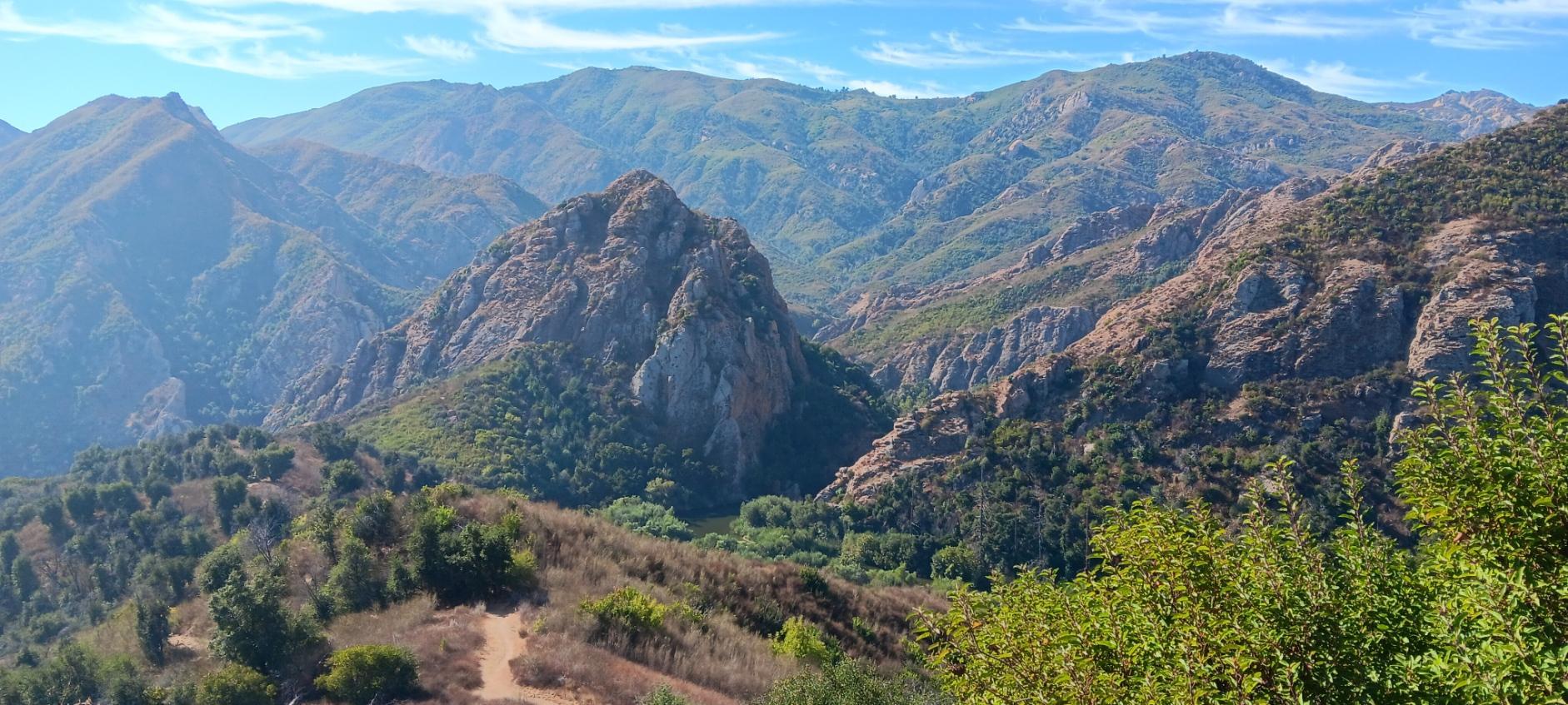 Panoramic view of rugged, green mountains and valleys under a blue sky.