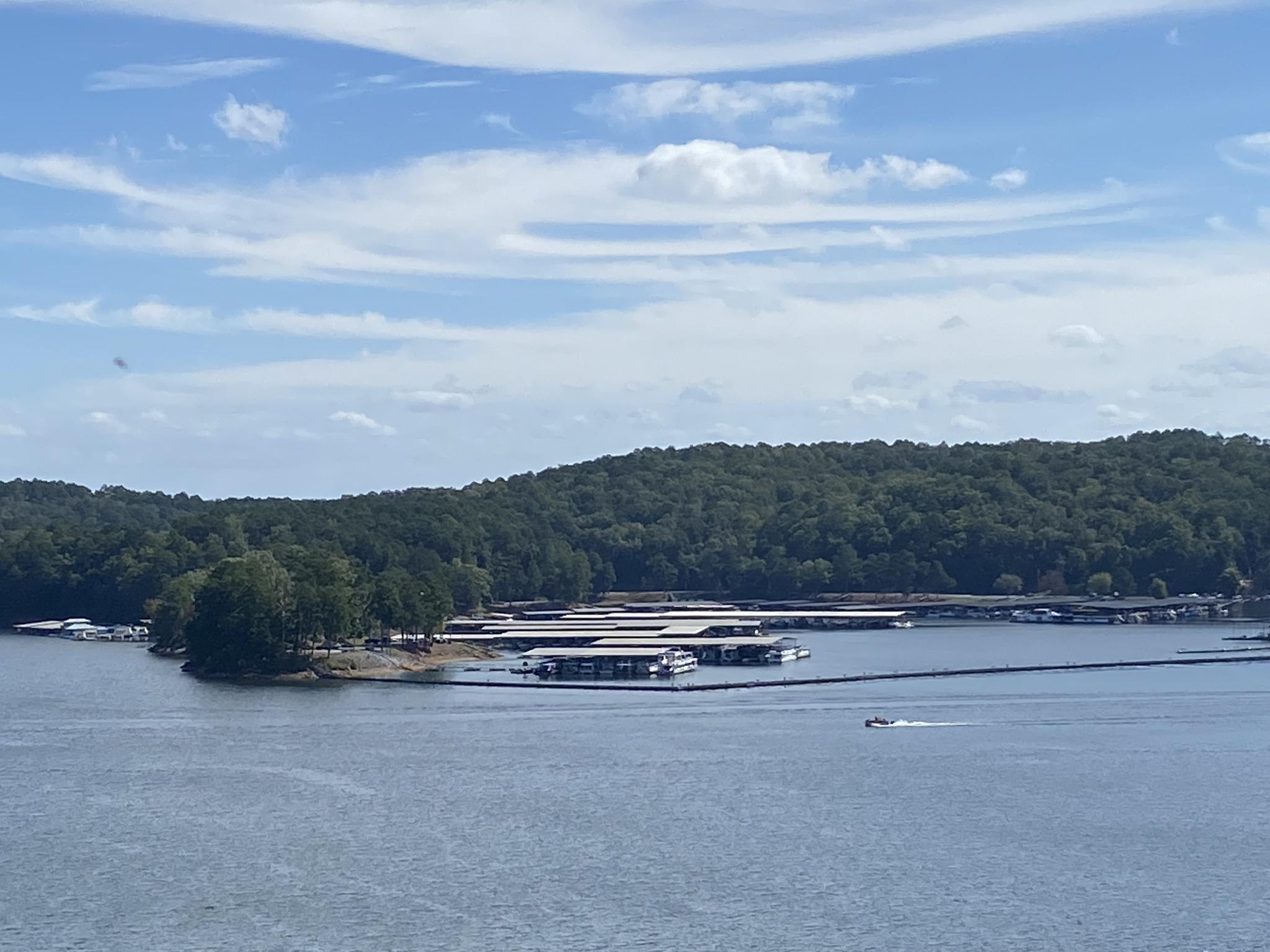 Wide lake view with boat docks, forested shoreline, and a small boat.