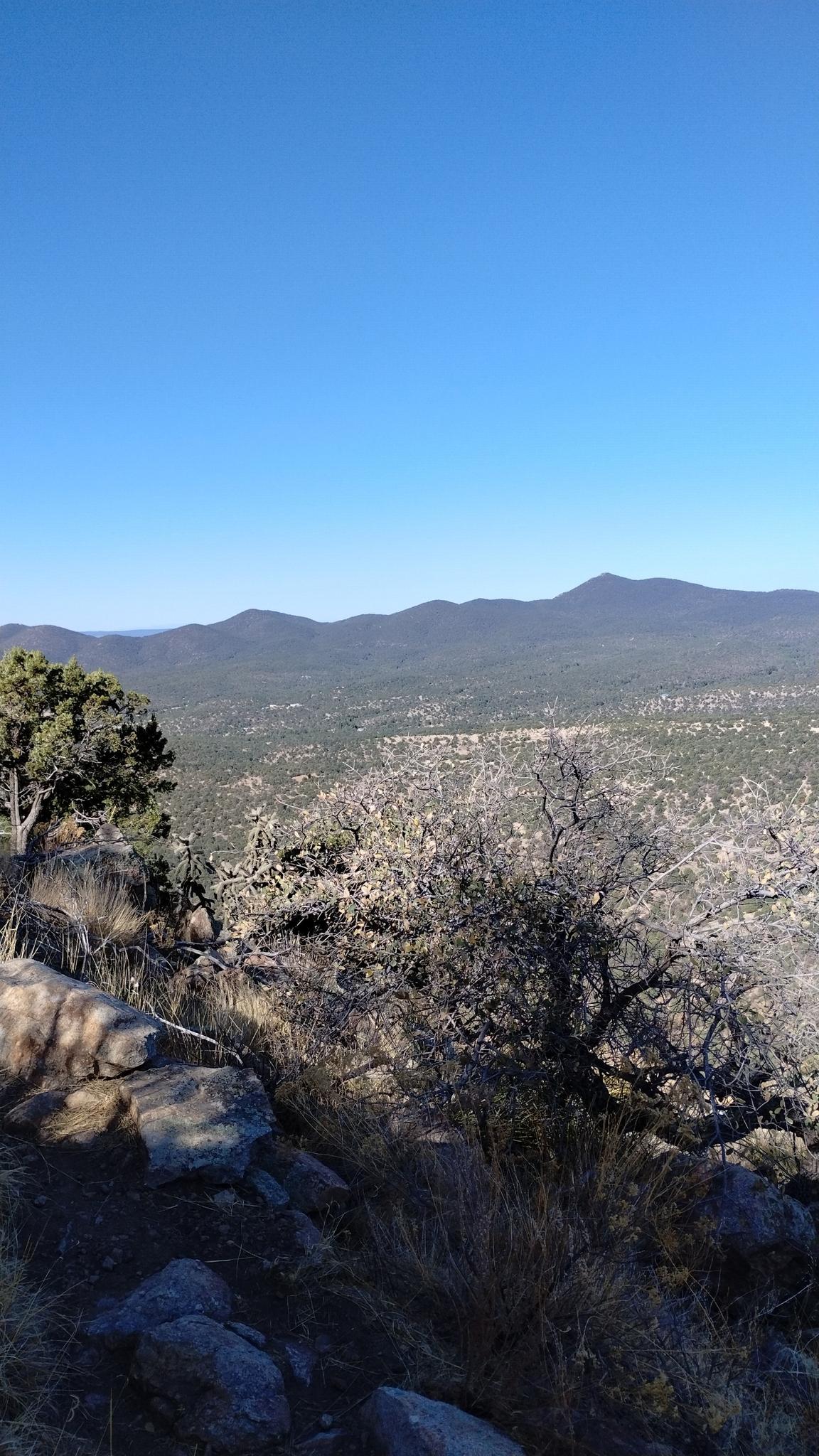 Vast, tree-dotted valley and distant mountains under a clear blue sky.