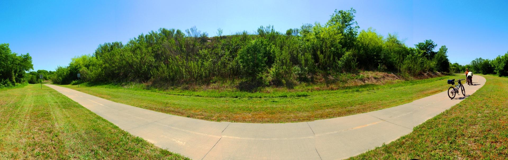 Bright paved path through green landscape with a bicycle under blue sky.