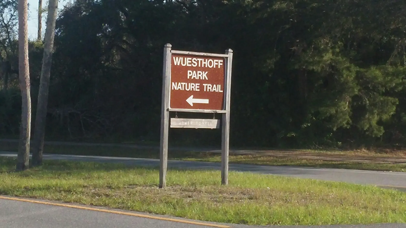 A brown park sign with white text and an arrow stands by a road.