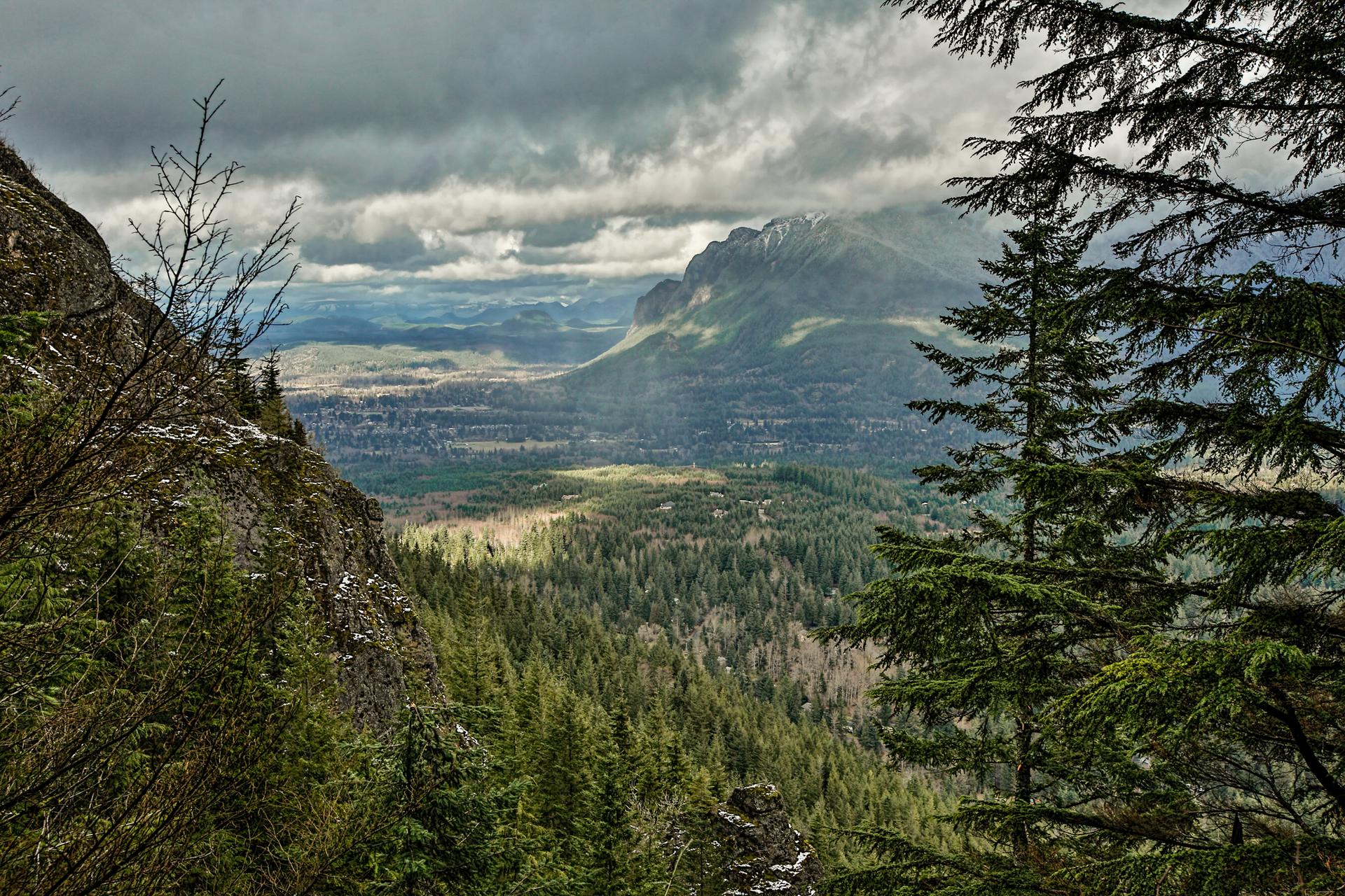 Overcast mountain valley with dense forest and distant peaks under cloudy skies.