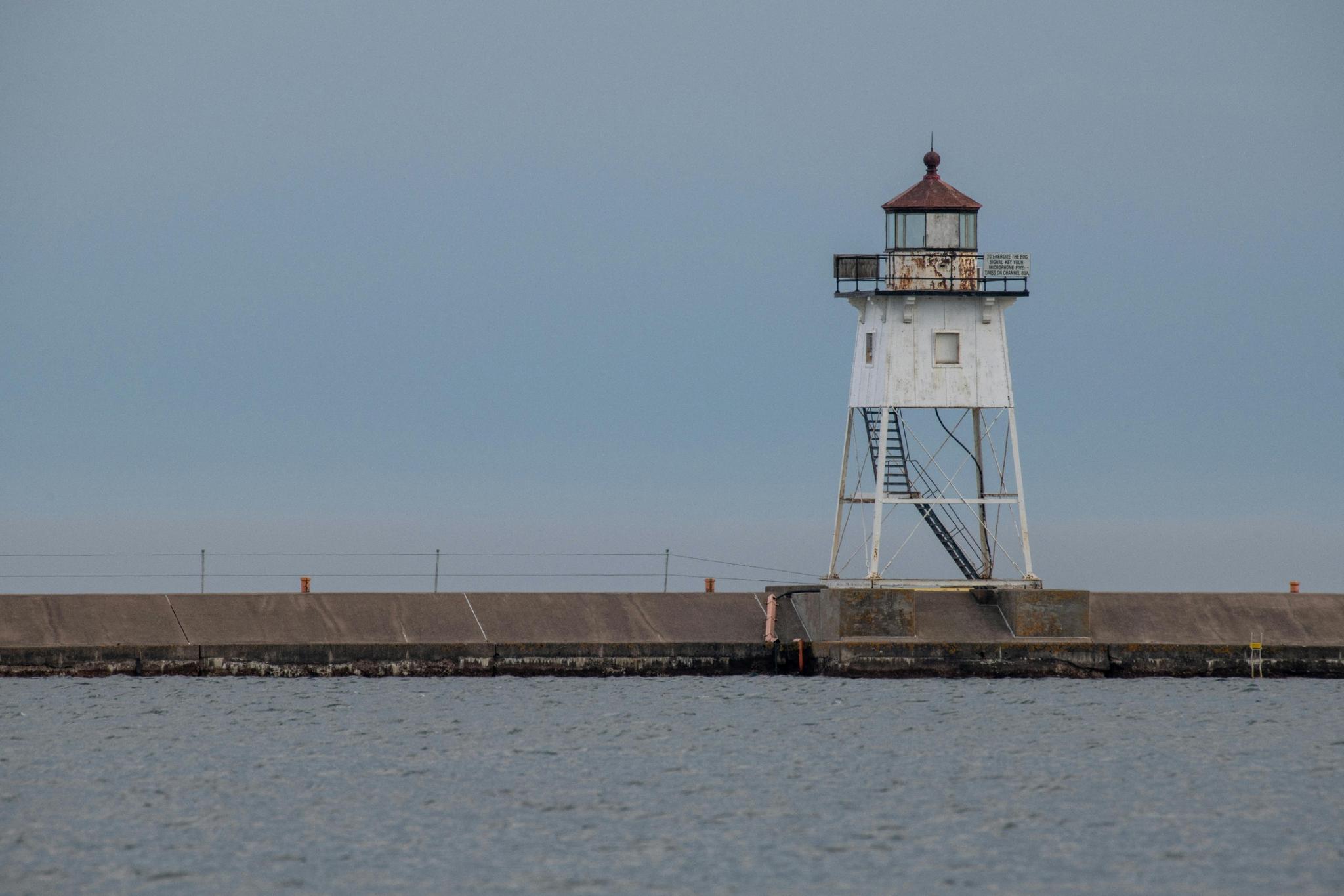 A white lighthouse with a dark roof stands on a concrete pier.