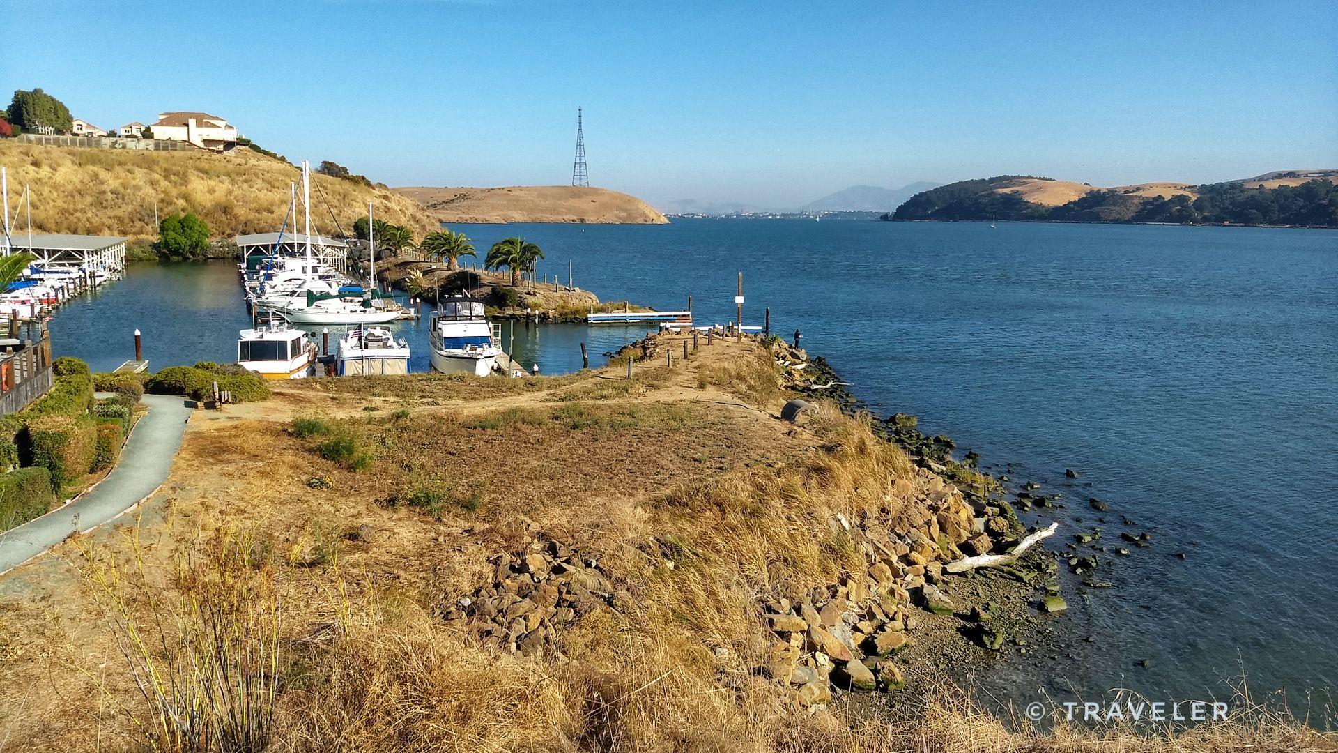 Sunny view of a marina filled with boats next to dry, rocky hills.
