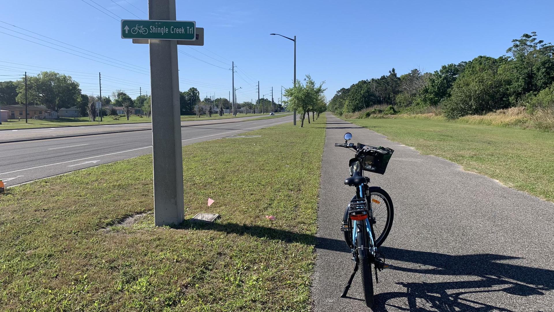Bicycle parked on a paved path next to a road on a clear, sunny day.