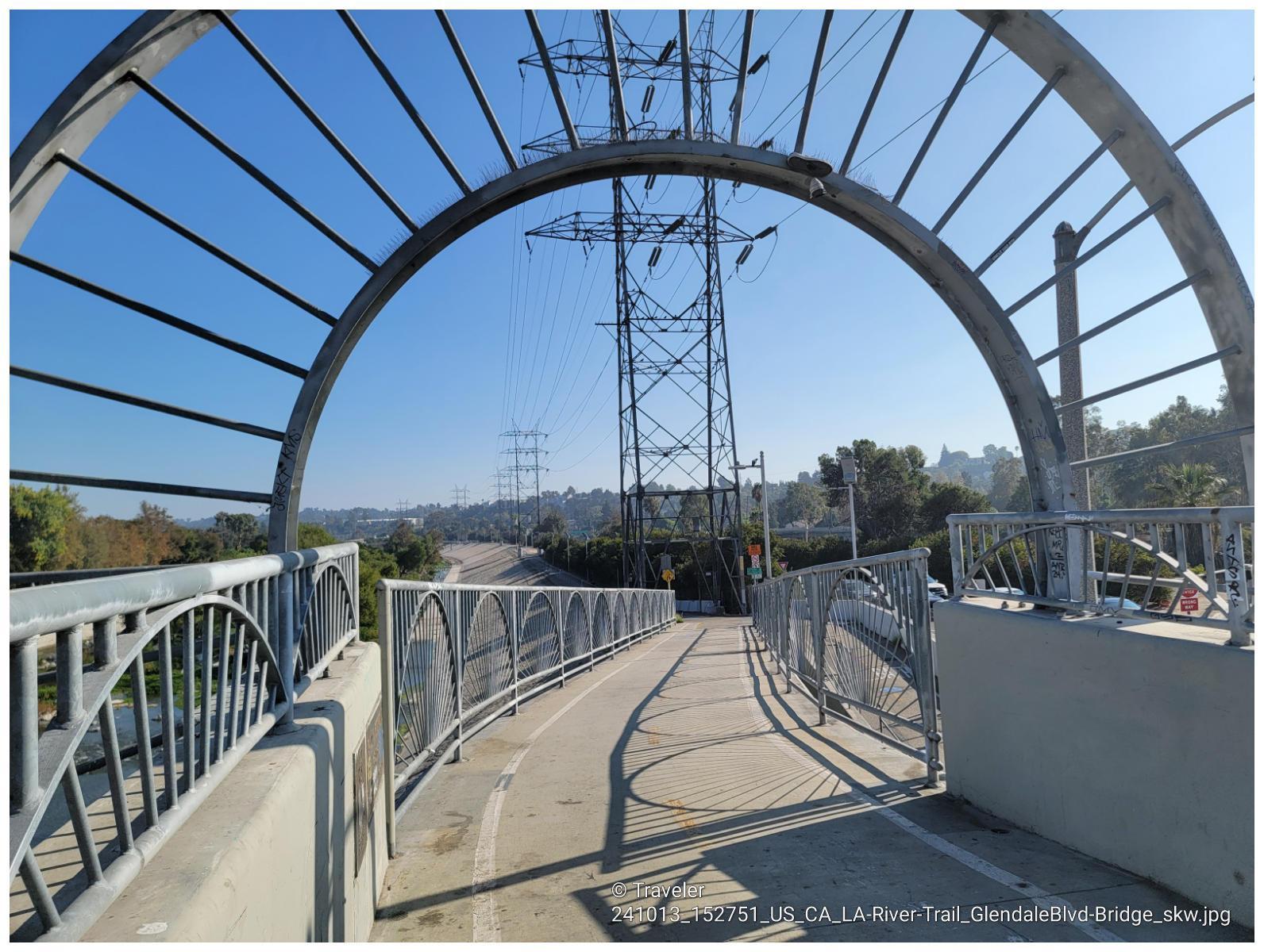 Arched pedestrian bridge with power lines and clear blue sky on a sunny day.