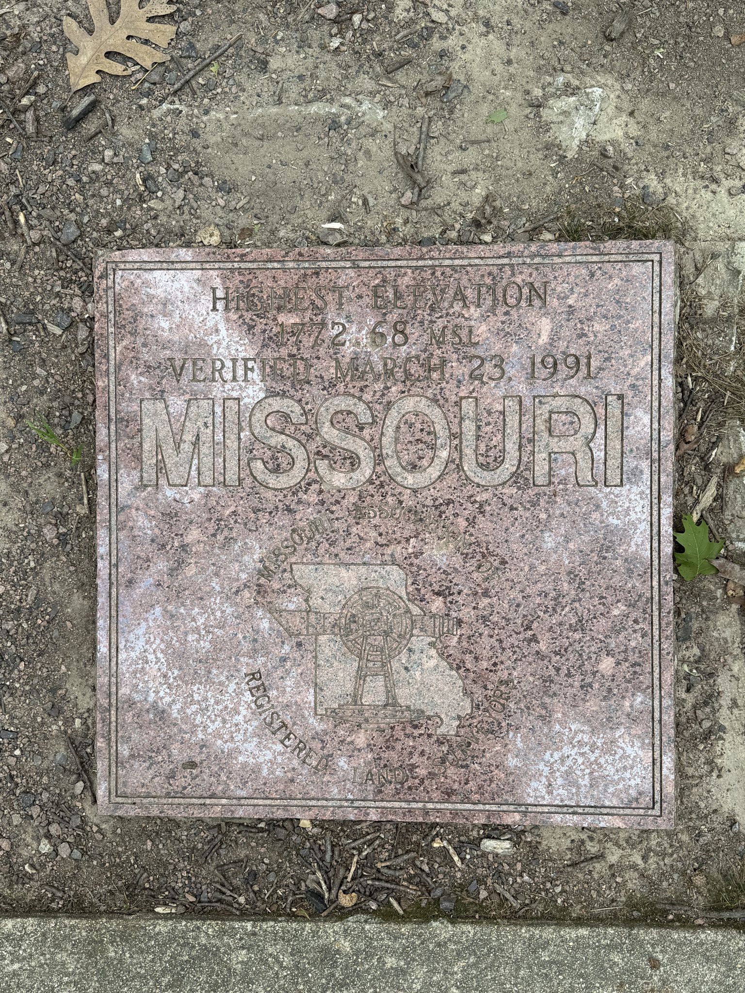 A square metal plaque with text and a state outline on the ground. - Ozark Trail: Taum Sauk Section