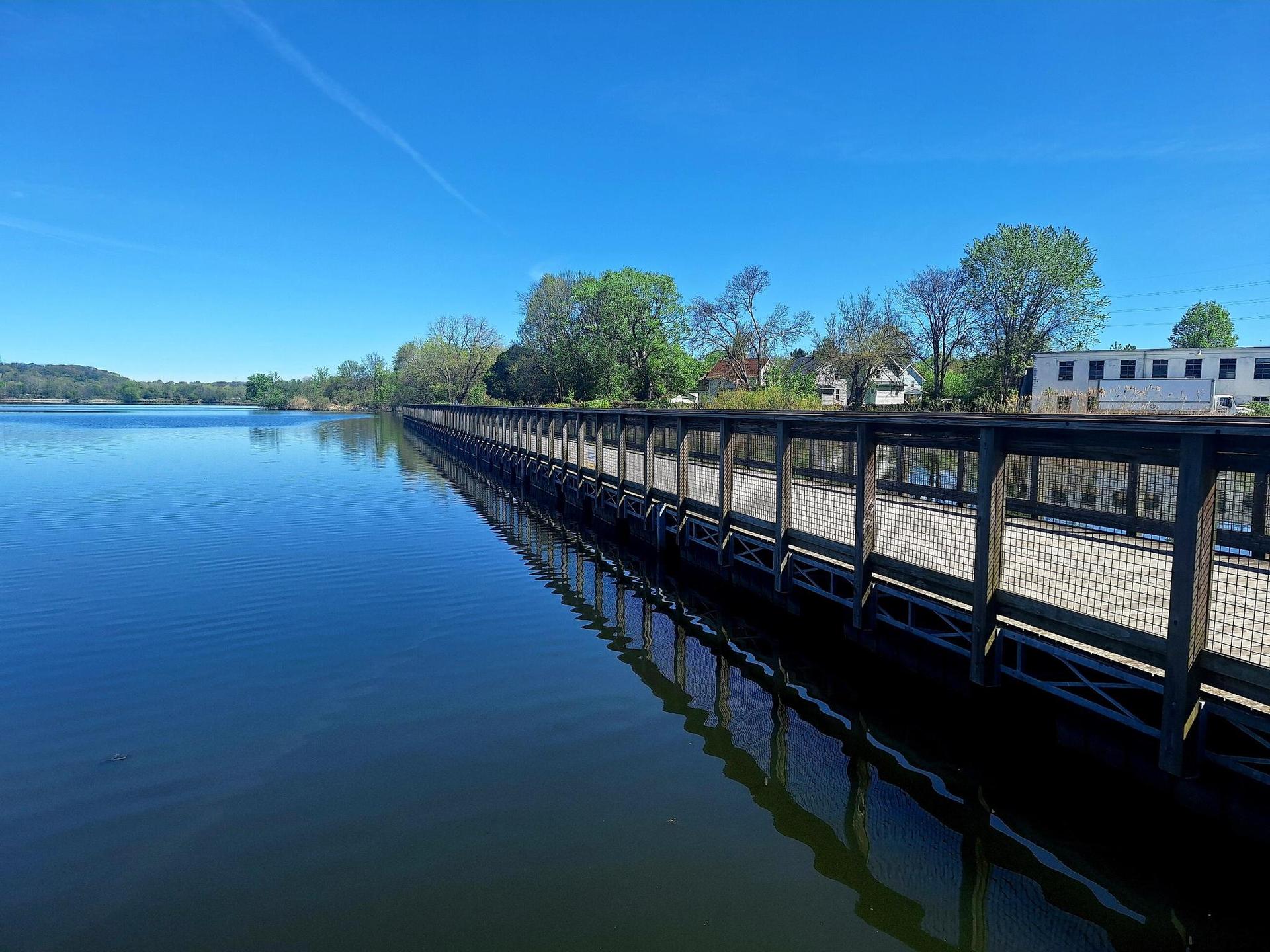Long wooden boardwalk over calm water under a bright blue sky.