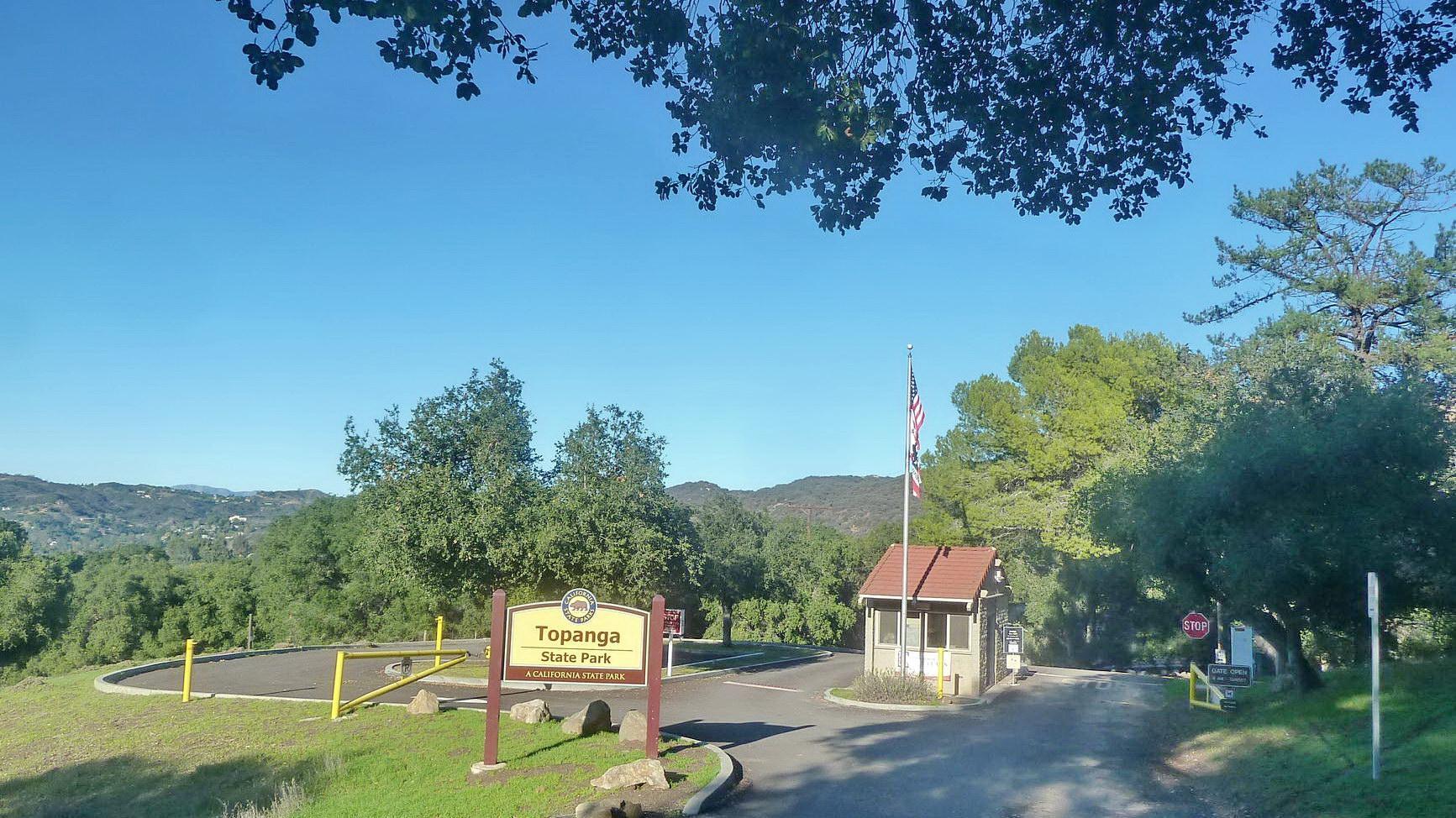 Park entrance sign and gate surrounded by green trees under a clear sky.