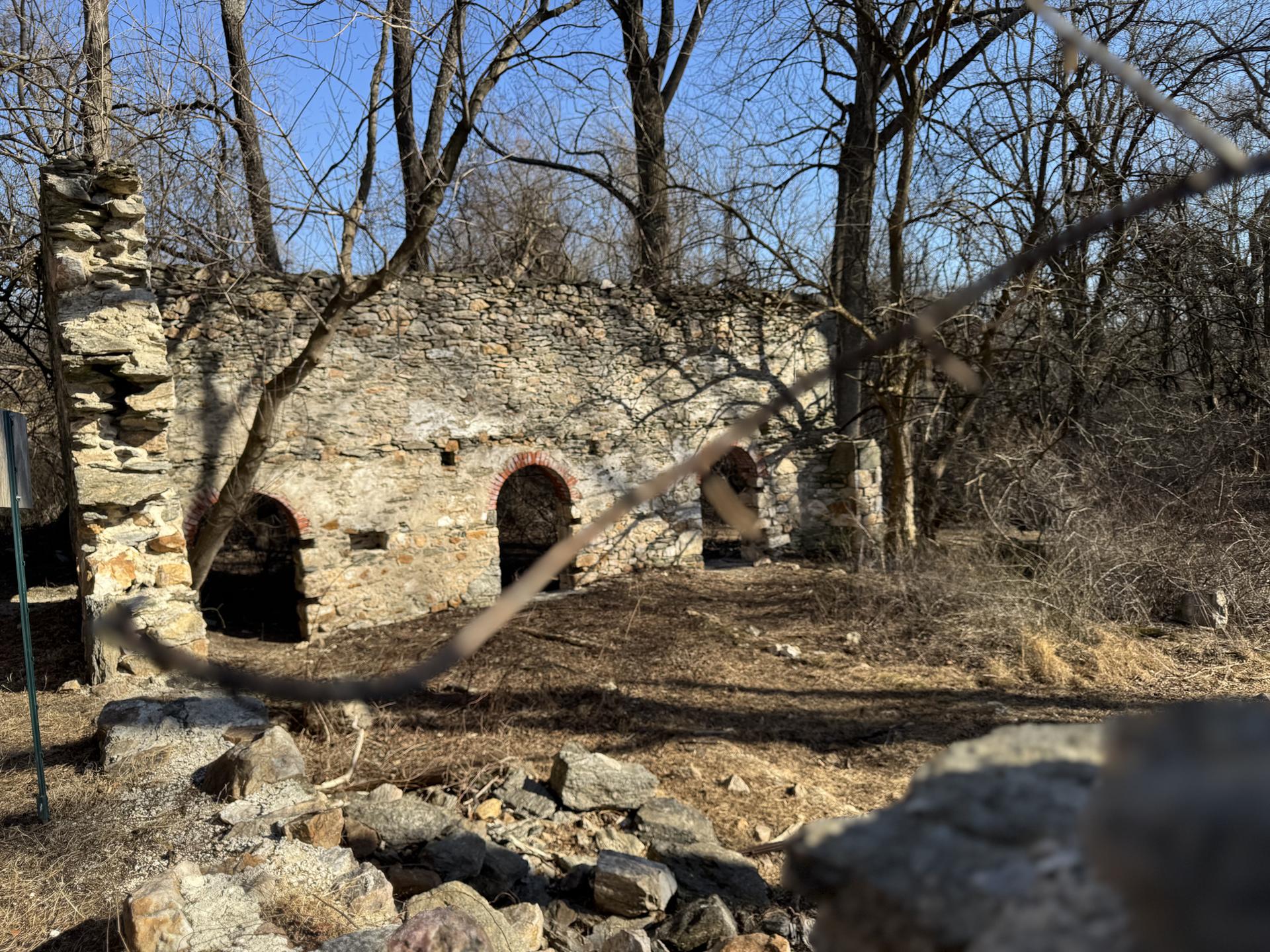 Old stone ruins with arched openings surrounded by bare trees on a sunny day.