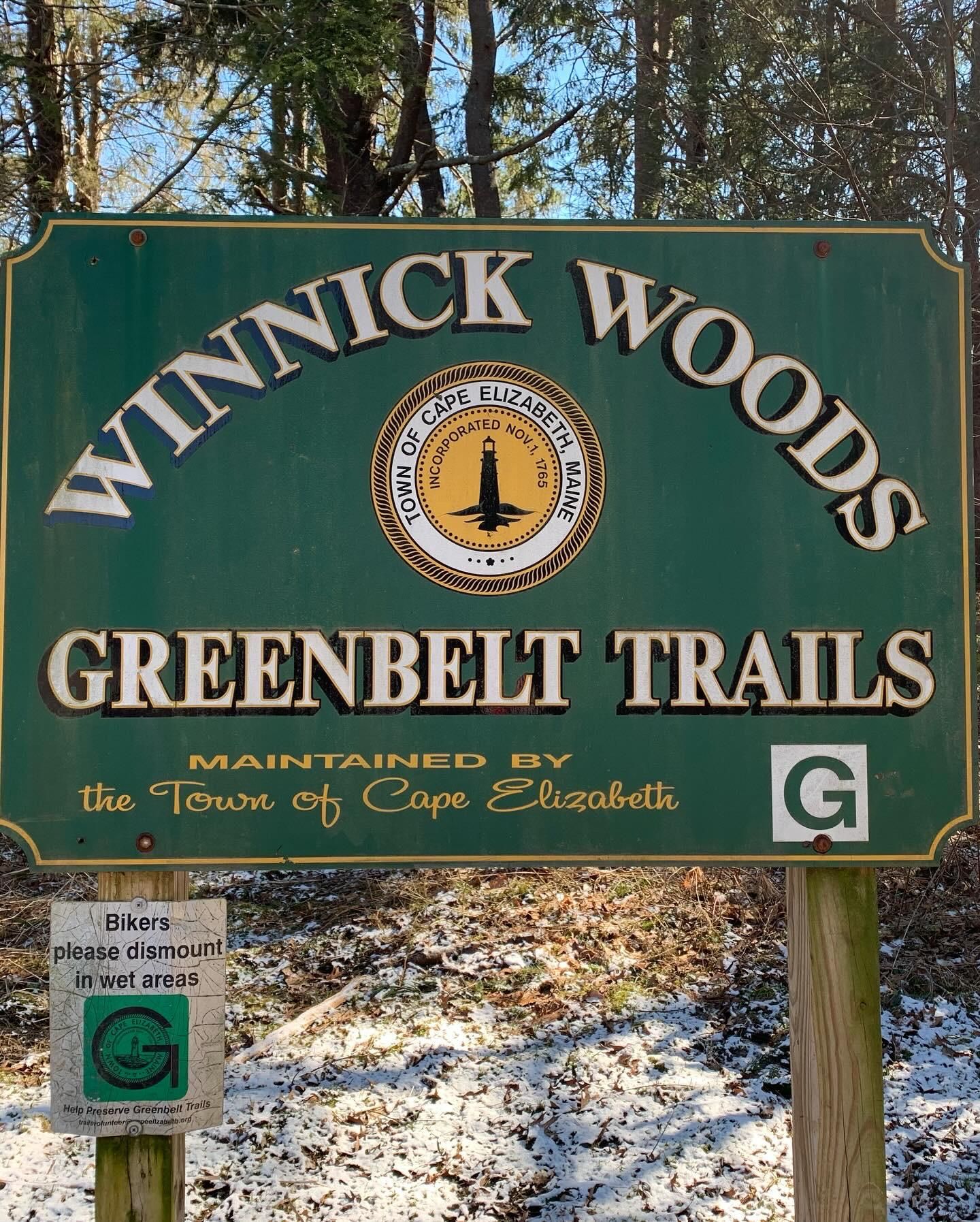 Green park sign with a circular emblem, set against snowy ground and trees. - Winnick Woods Long Loop
