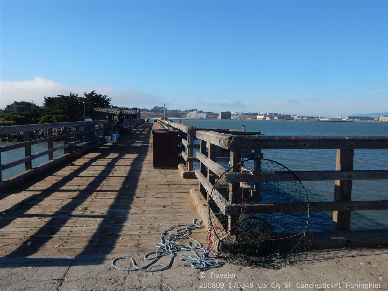 Wooden pier with fishing net and ropes, overlooking a bay and distant city.