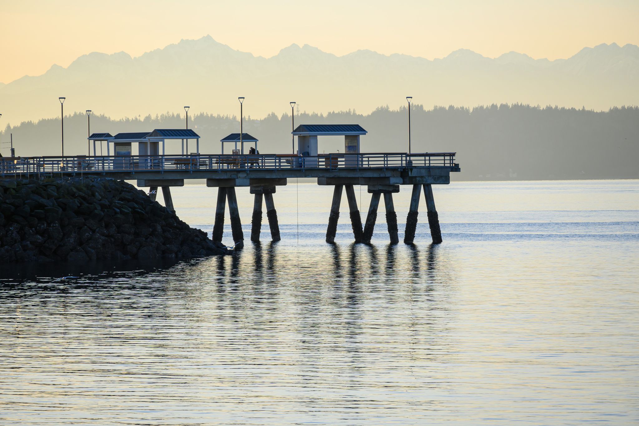 A long pier extends into calm water with distant hazy mountains at sunset. - Olympic Beach – Brackett's Landing loop from Edmonds
