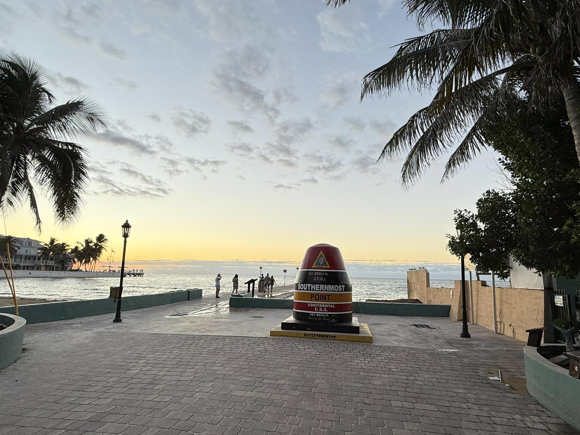 Colorful monument at sunset by the ocean, with people gathered.
