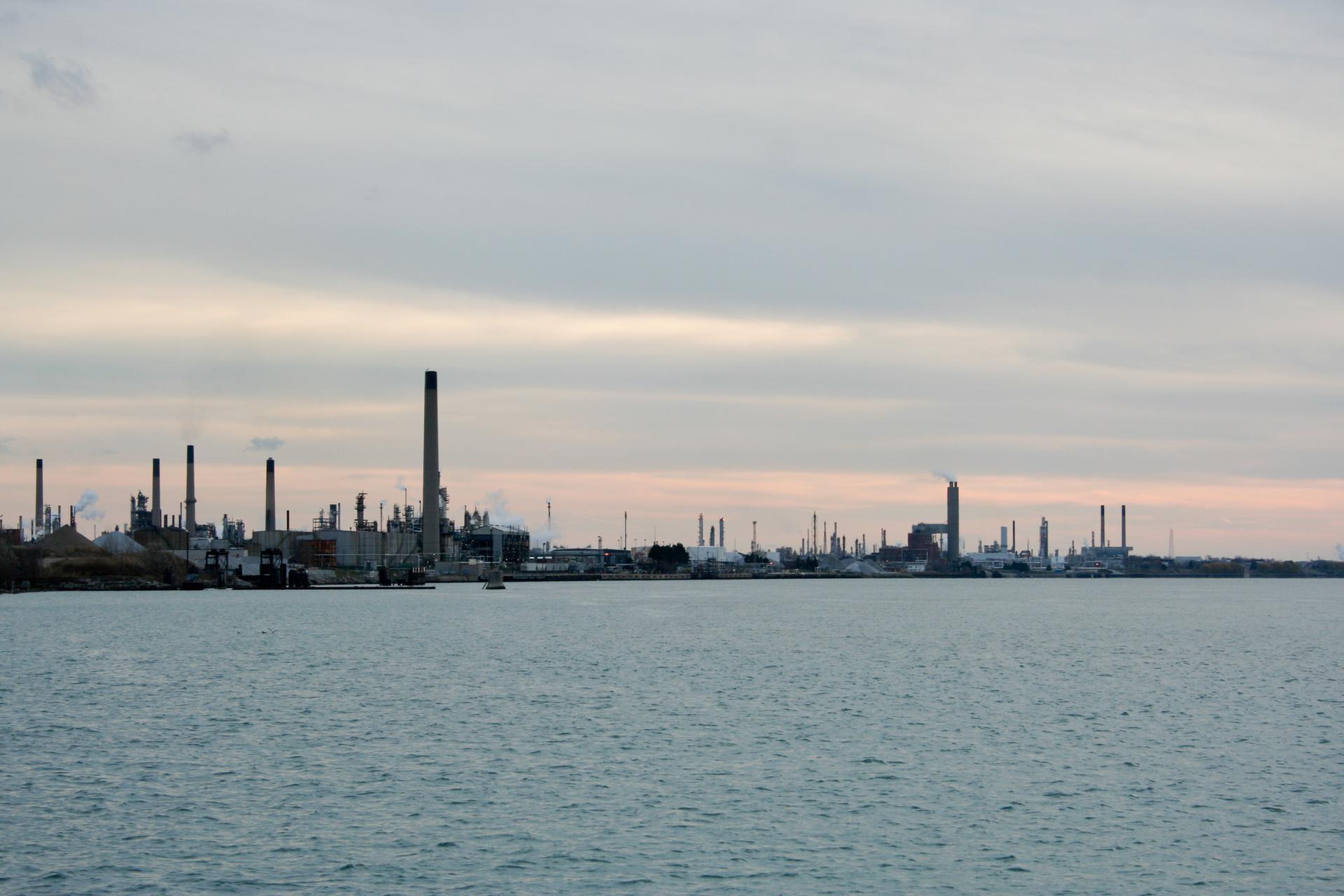 Industrial complex with many smokestacks along a waterfront under an overcast sky.