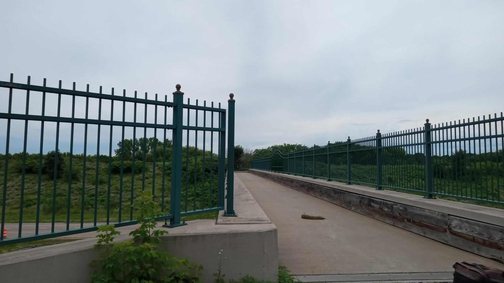Long metal fence alongside a paved path under an overcast sky.