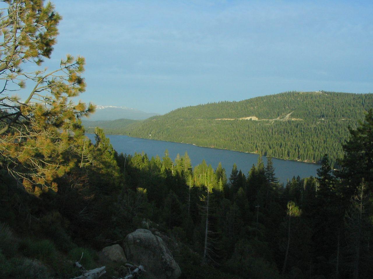 Scenic view of a large lake surrounded by green forested hills at sunset.