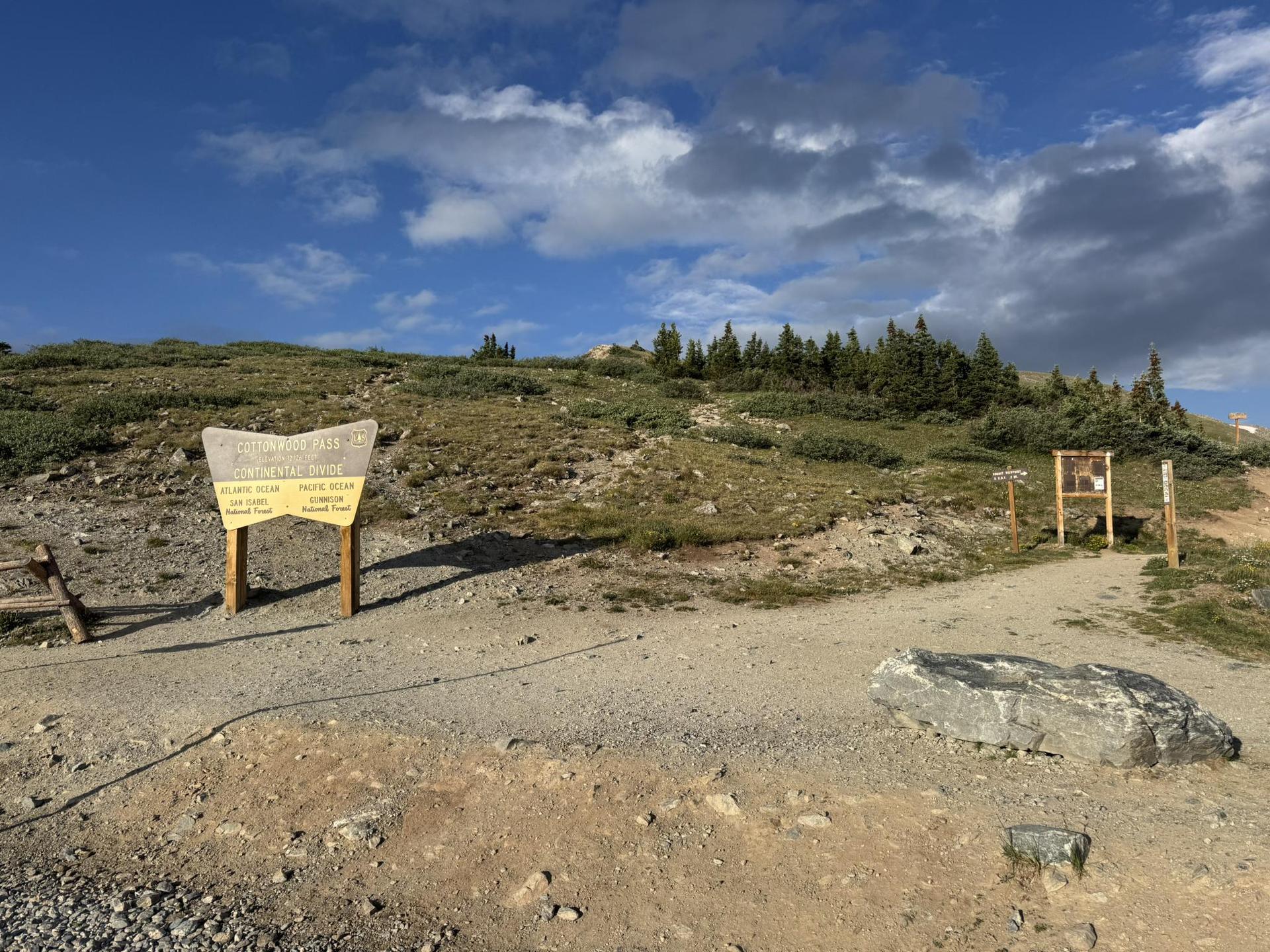 Two wooden signs on a dirt path leading up a grassy hill.
