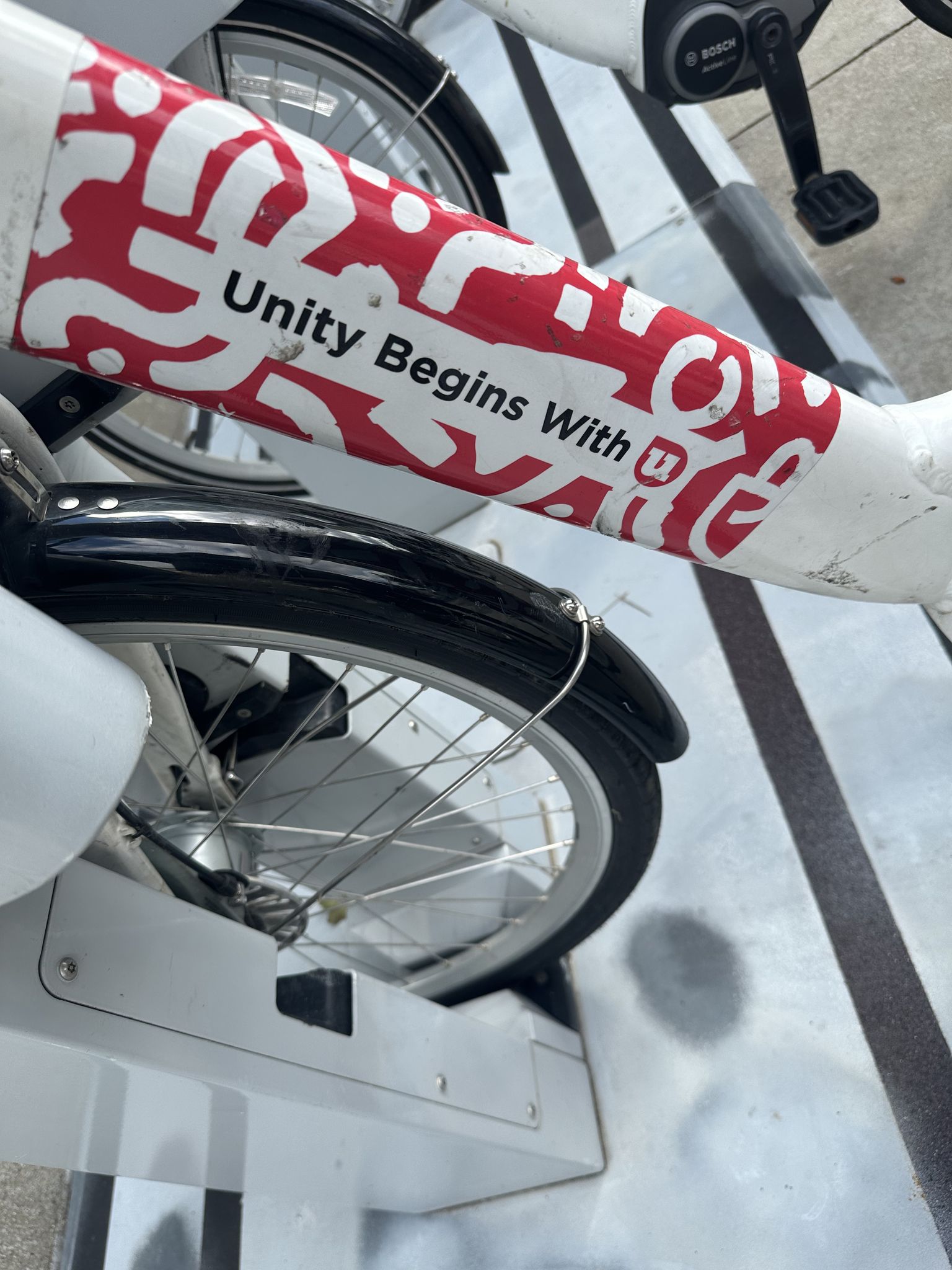 Close-up of a white bicycle frame with "Unity Begins With" text. - Lake Monona Loop