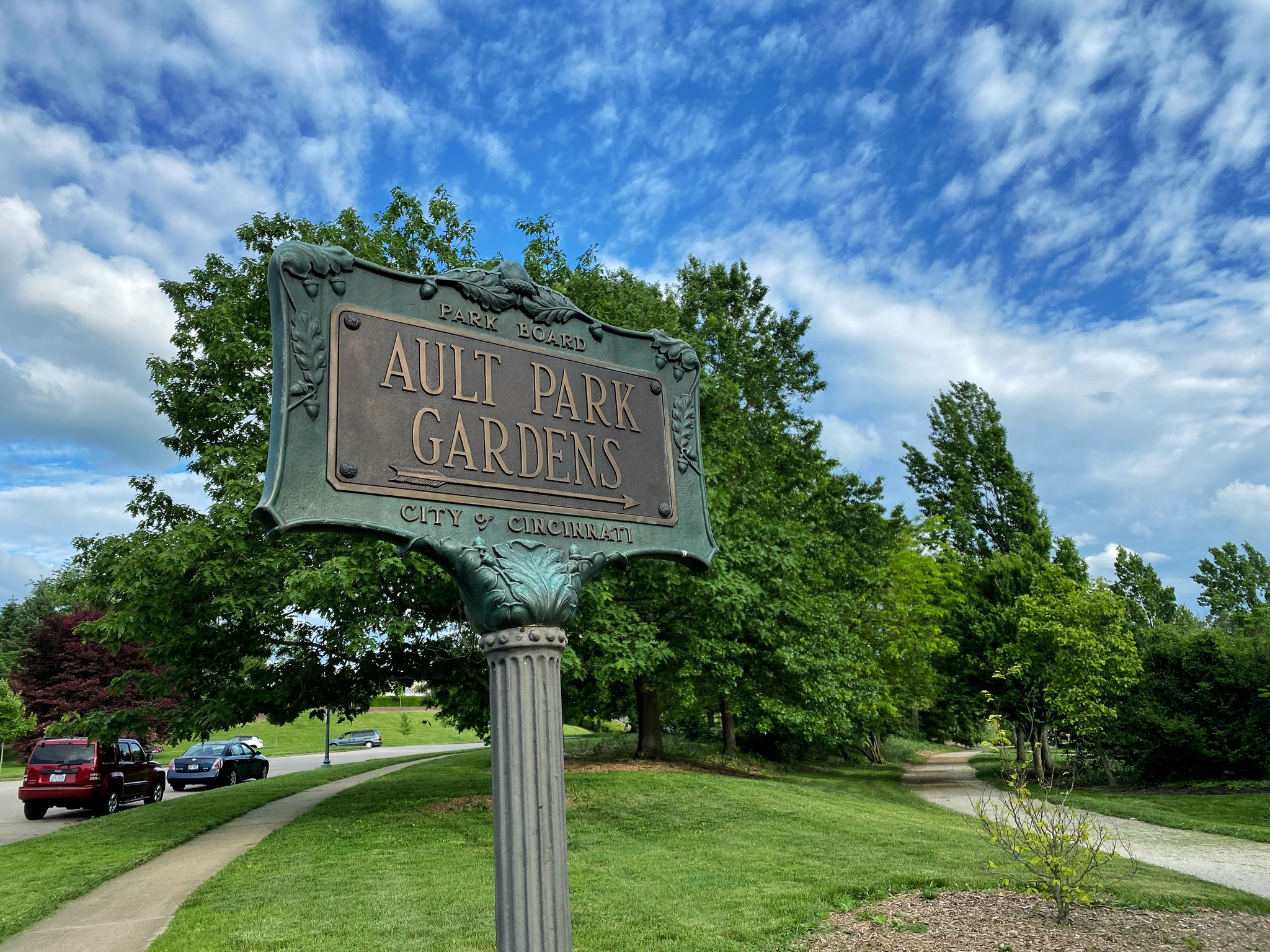 A bronze sign on a pole with green trees and a bright blue sky. - Ridge, Bur Oak, Cliff and Tree Trail Loop