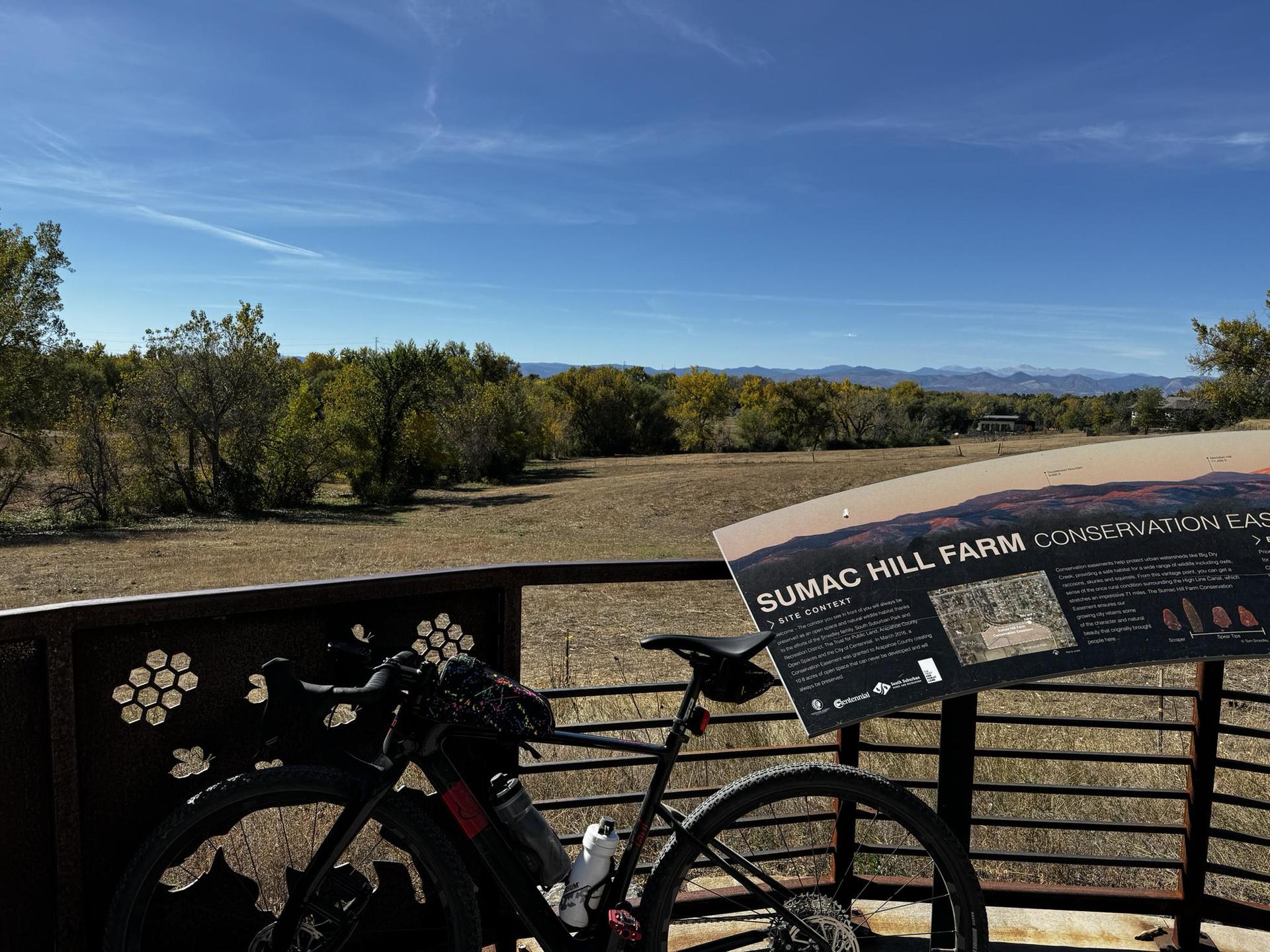 A bicycle and sign overlook a sunny field with distant mountains.