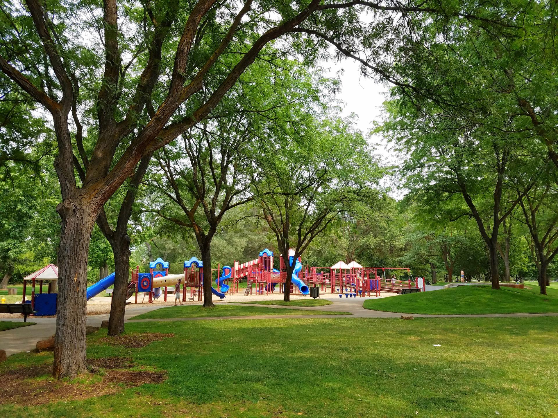 A colorful playground with slides and swings nestled among large shade trees.