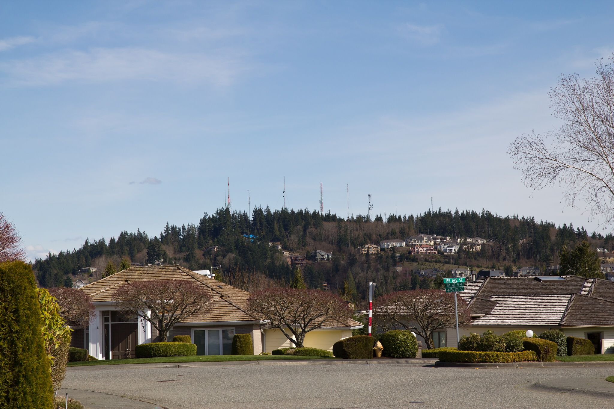 Residential street with houses and a forested hill topped with antennas. - Summit Clubhouse loop from Lake Sammamish State Park