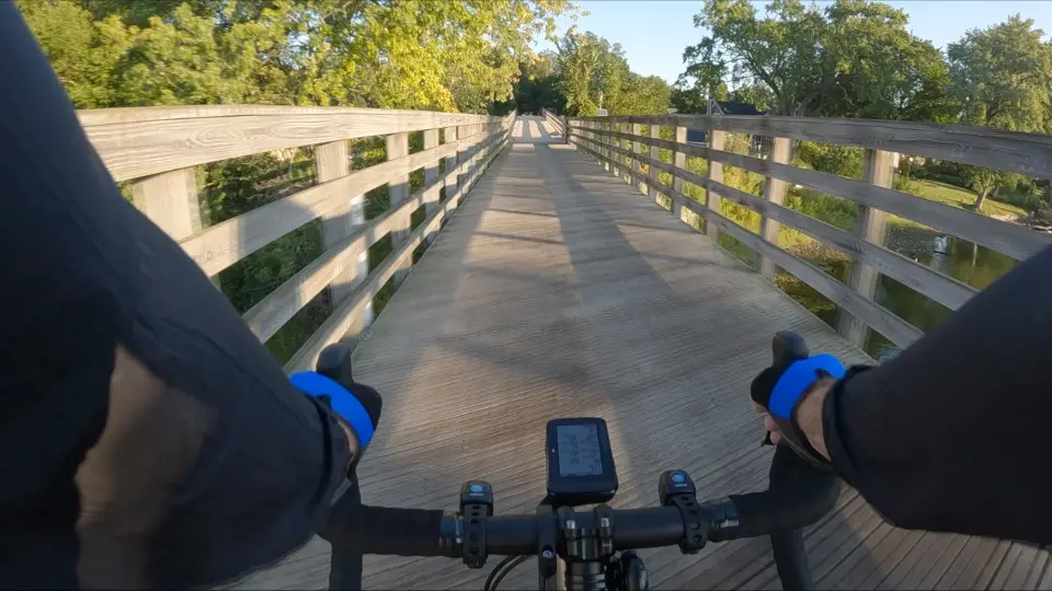 Cyclist's view riding on a sunny wooden bridge through green trees.