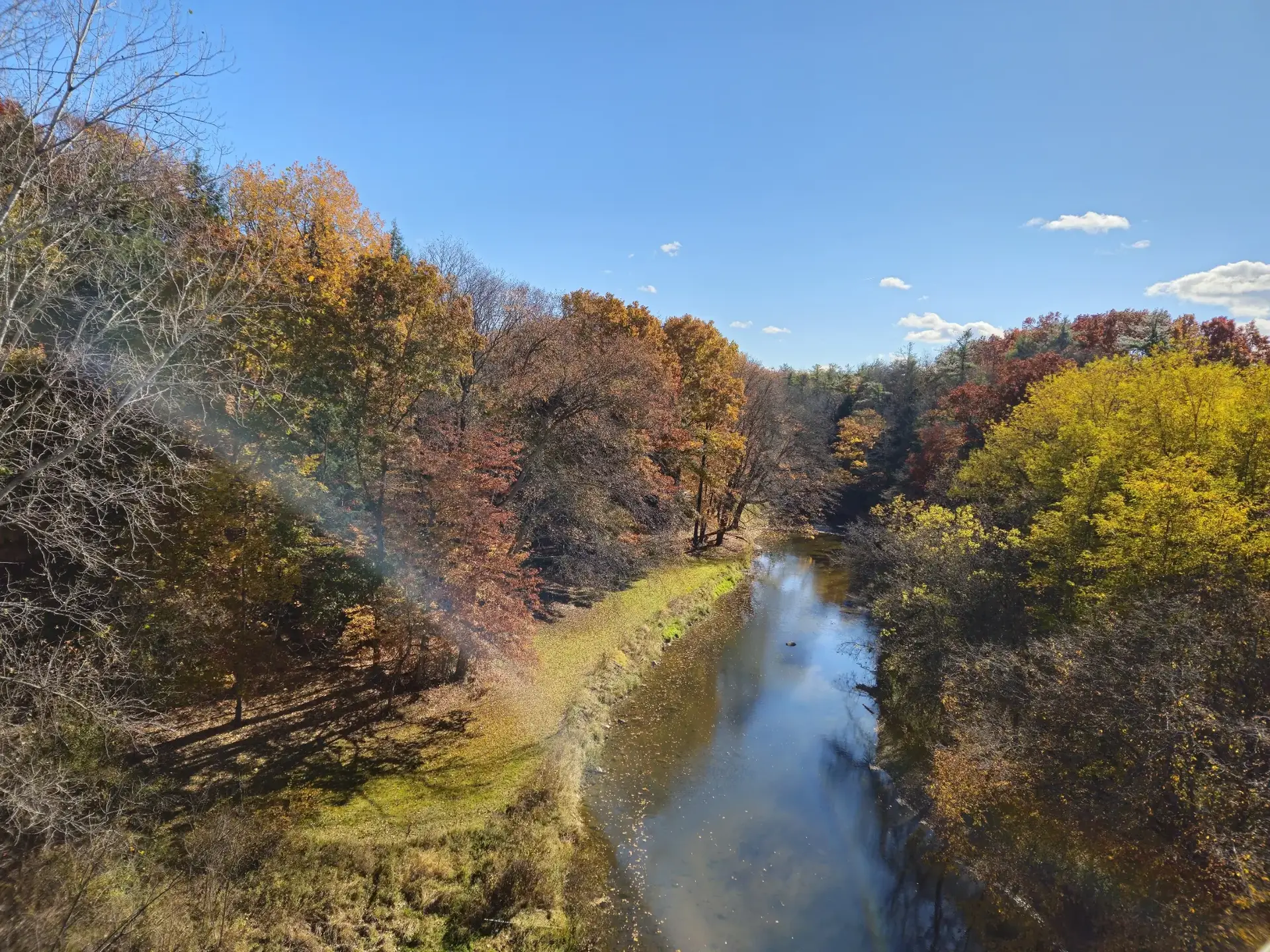 A river winds through a vibrant autumn forest under a clear blue sky.