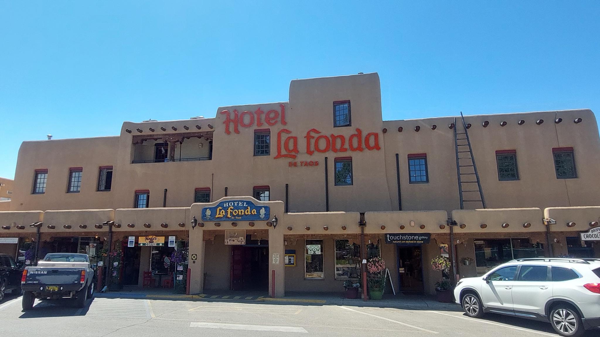 A large, multi-story adobe-style building with shops and parked cars under clear skies.