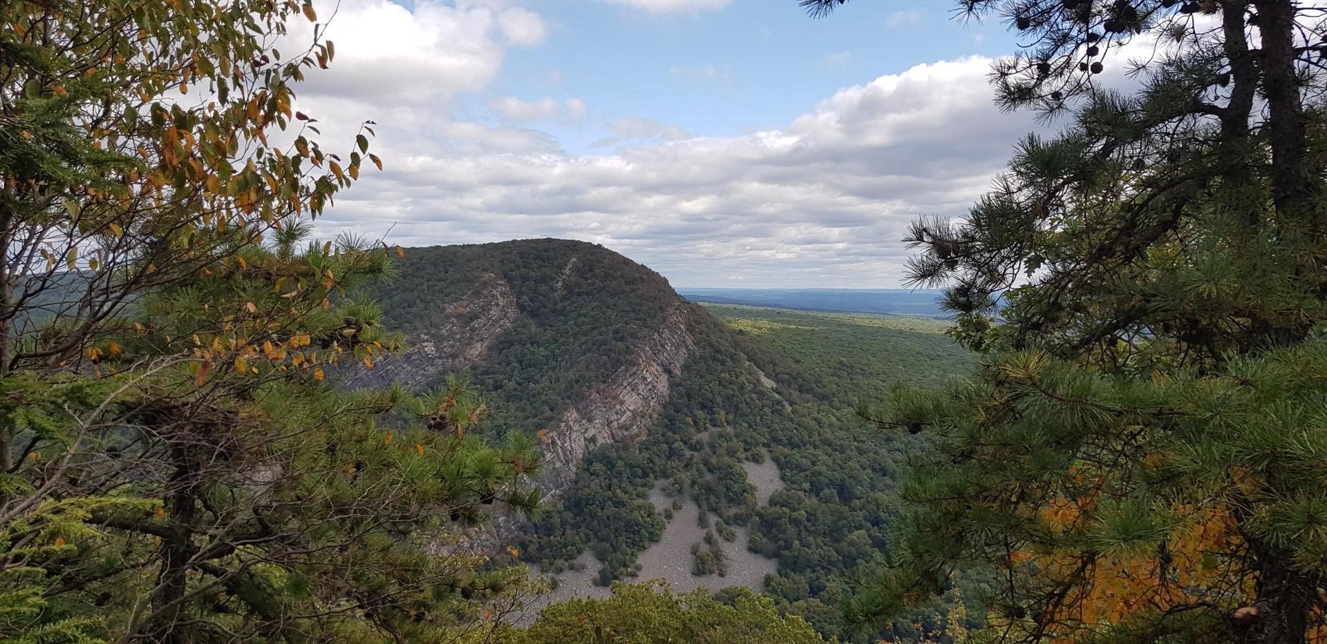 A vast forested mountain valley under a partly cloudy sky.