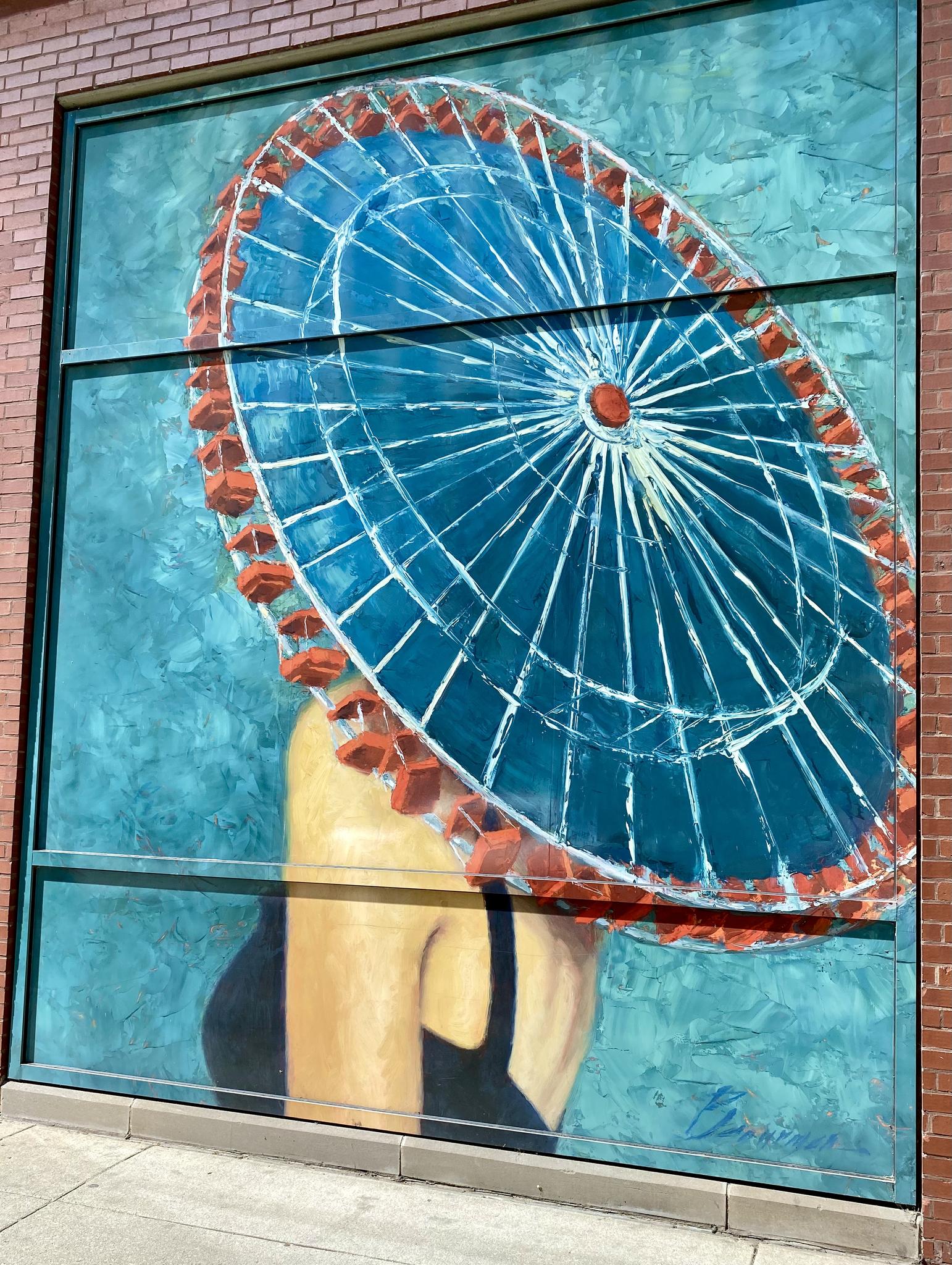 Colorful mural on a building wall depicting a person with a large blue wheel.