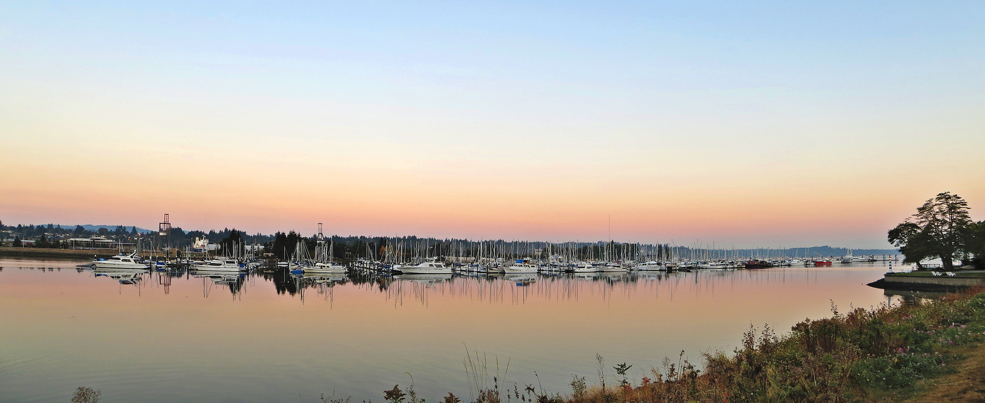 A tranquil marina filled with boats at sunset, reflecting in calm water.
