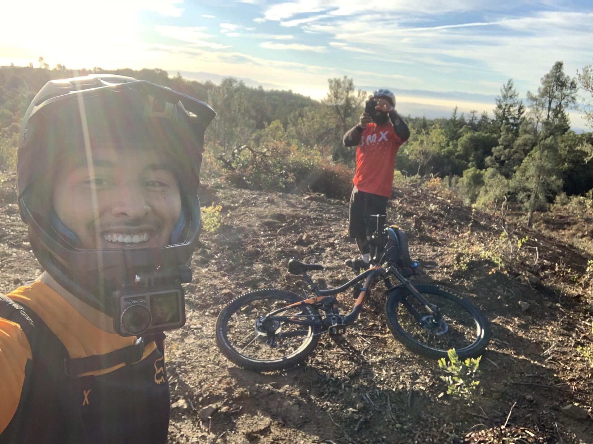 Two men with mountain bikes on a sunny, dry hillside at golden hour.