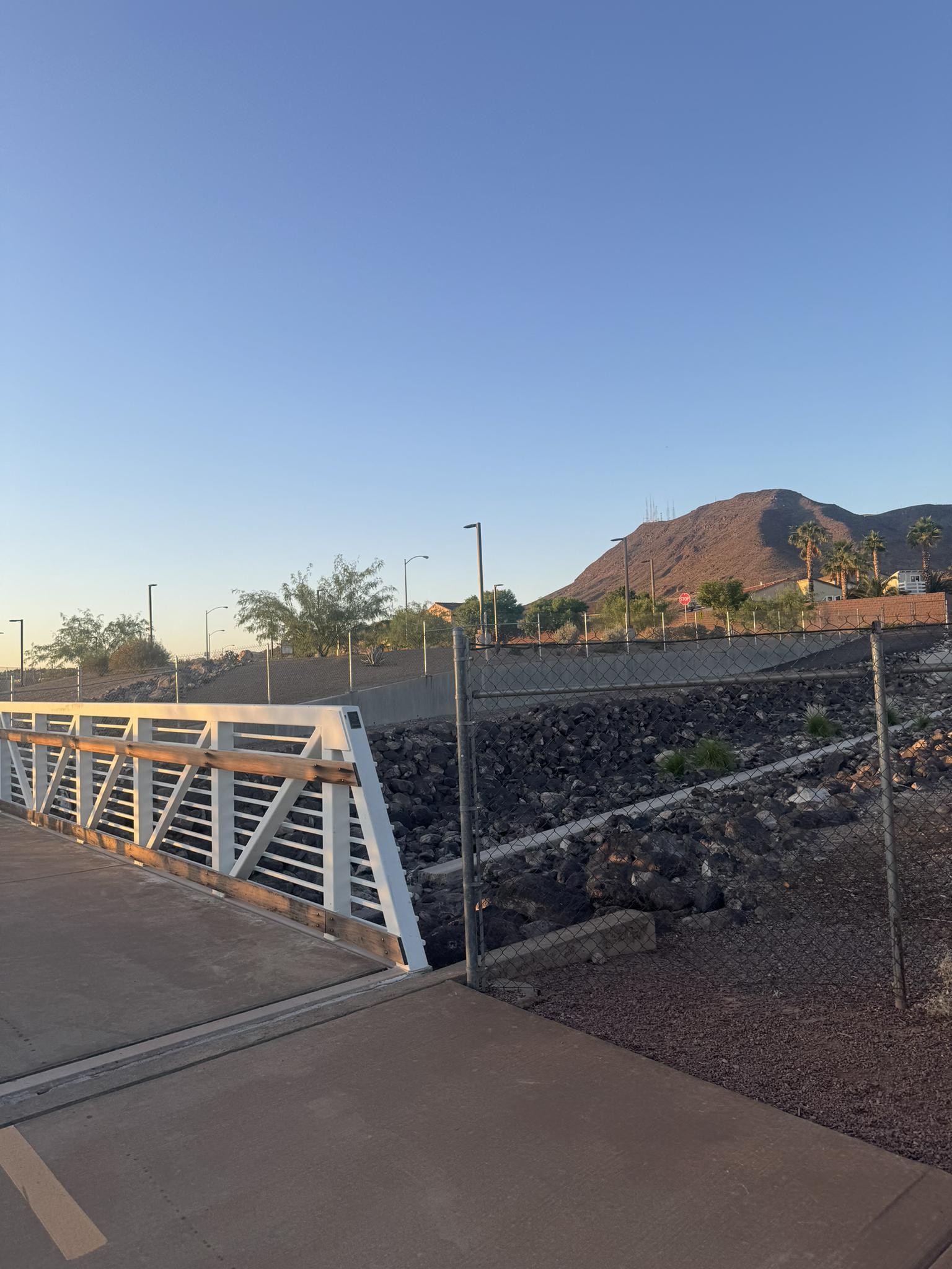 Pedestrian bridge over rocky terrain, distant mountain under golden light.
