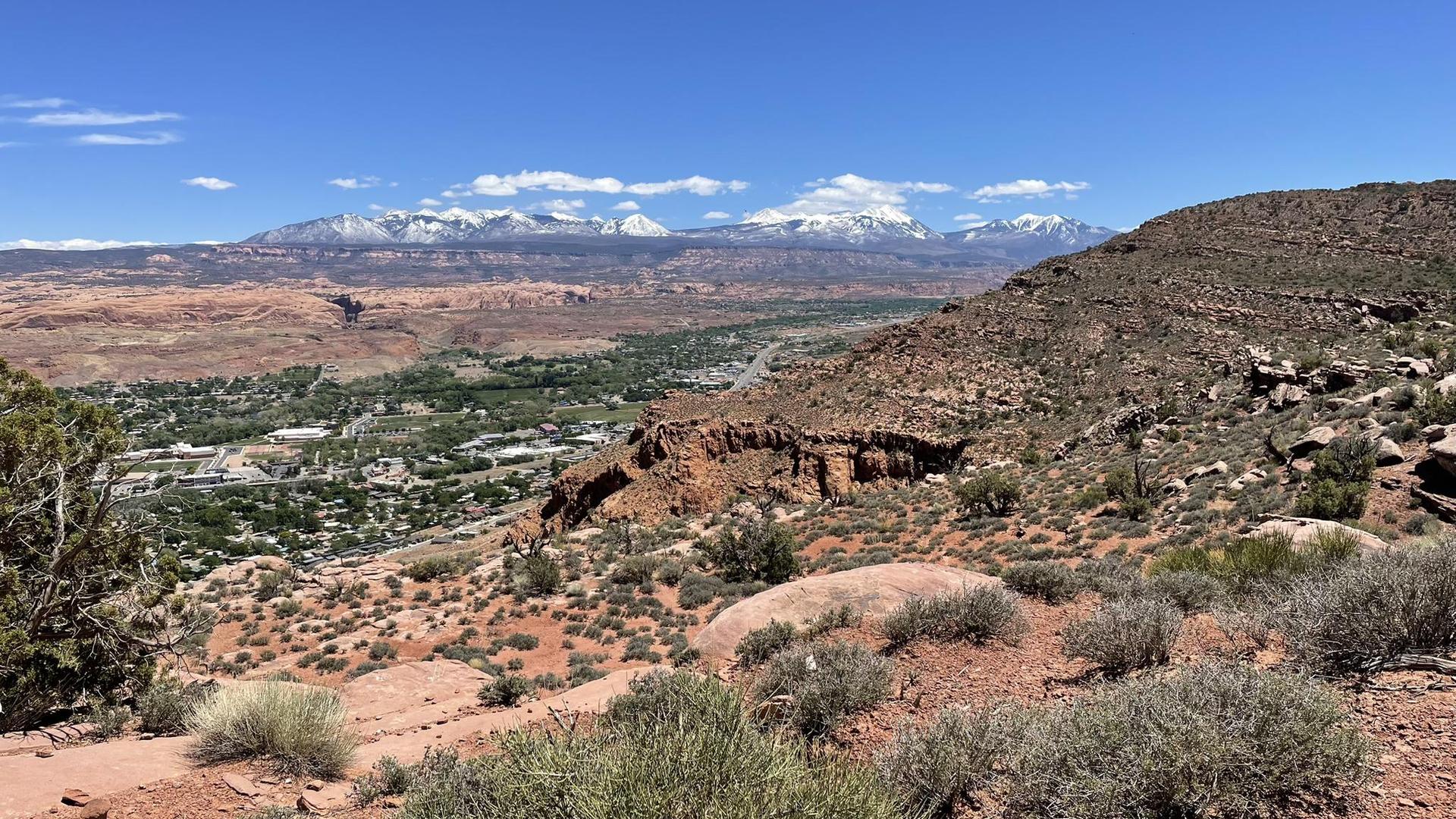 Panoramic view of a green valley with buildings, backed by snow-capped mountains.