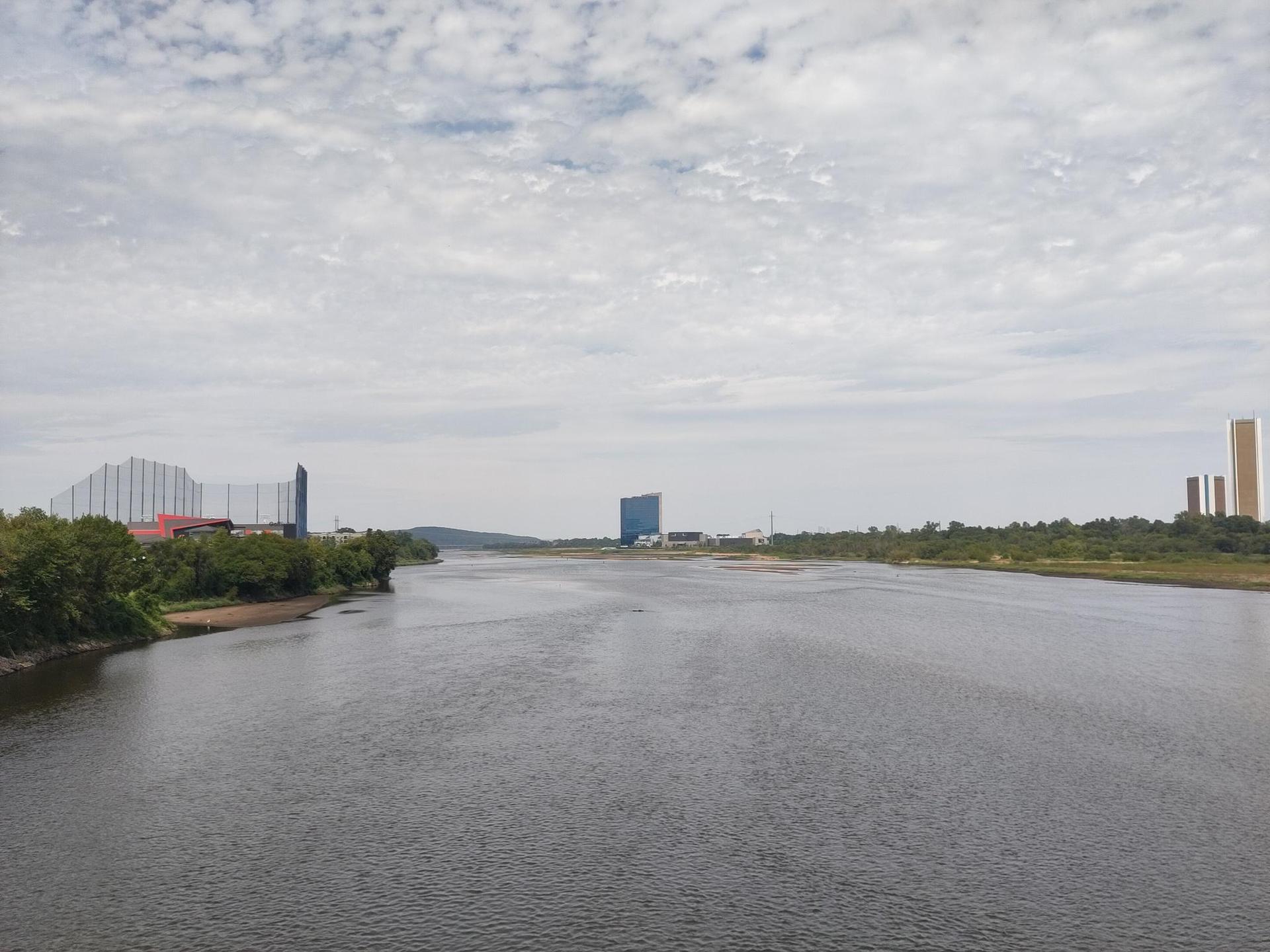 Wide river with buildings and trees on banks under a cloudy sky.