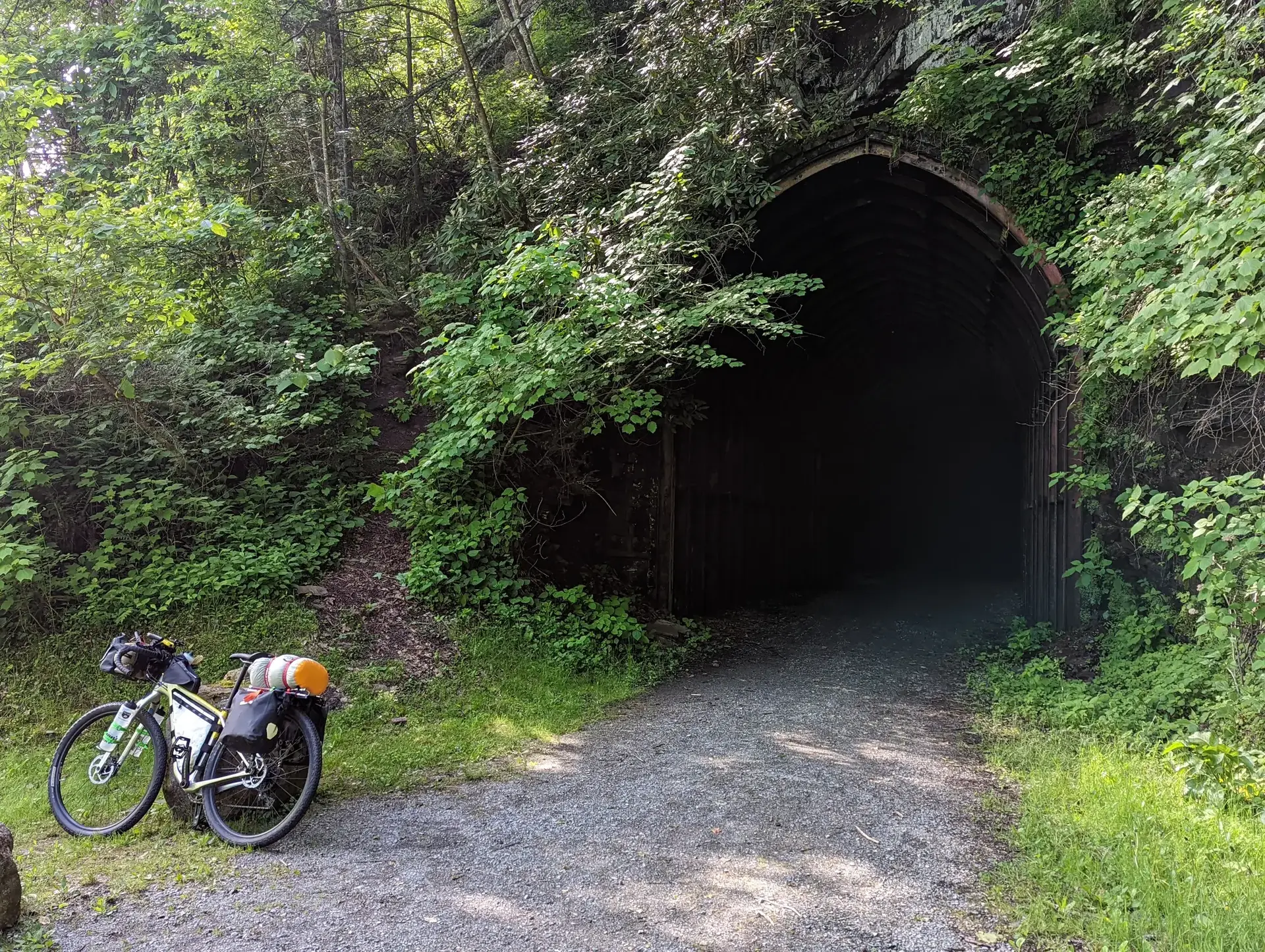 A touring bicycle rests near a dark tunnel entrance in a wooded area.