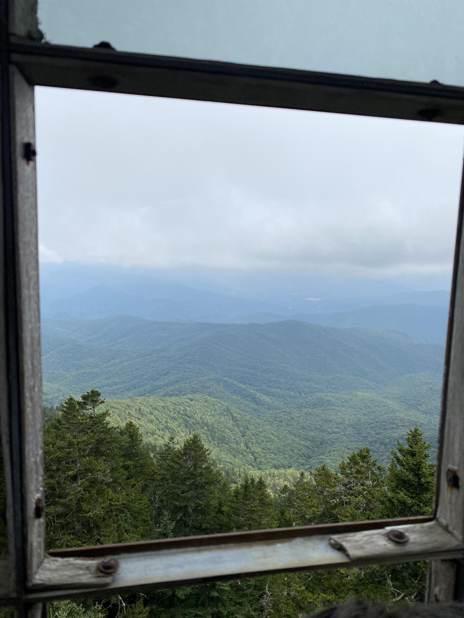 A cloudy mountain range view seen through a rustic window frame.