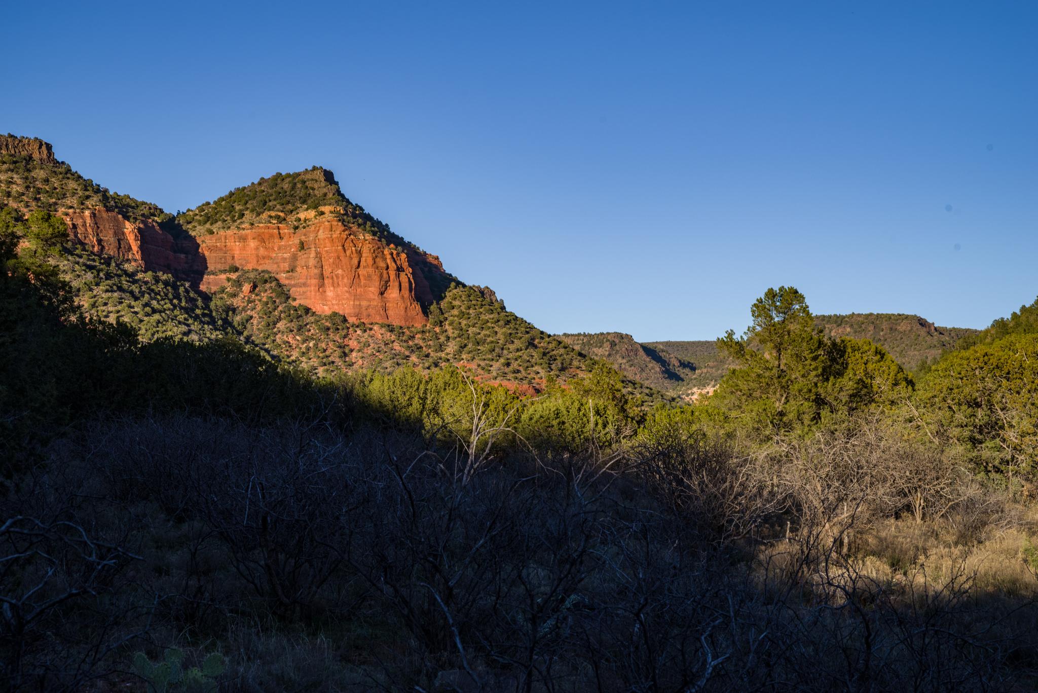 Red rock mountains bathed in sunlight, with shadowed hills in the foreground.