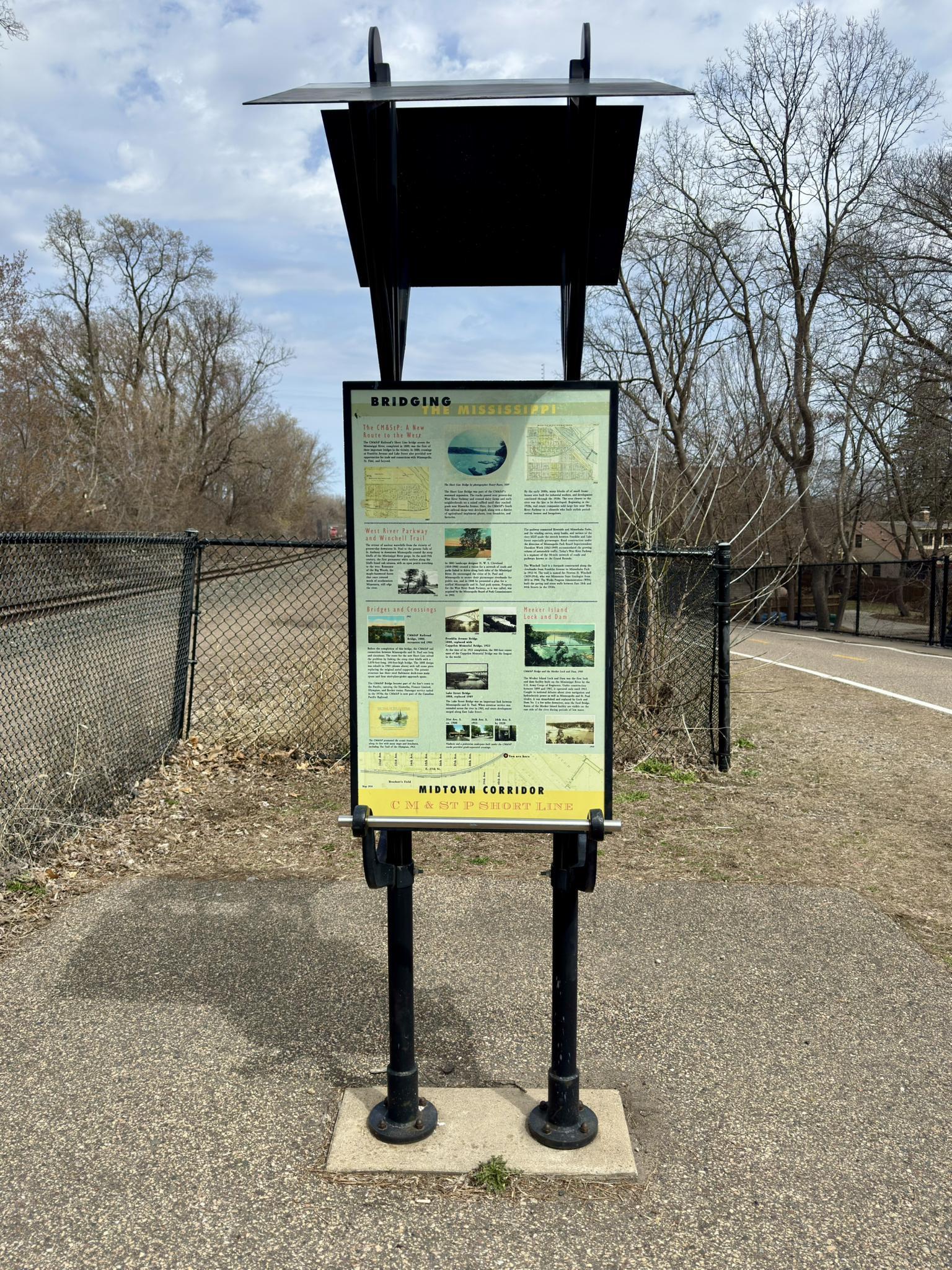 An outdoor information sign with a black canopy next to a paved path.